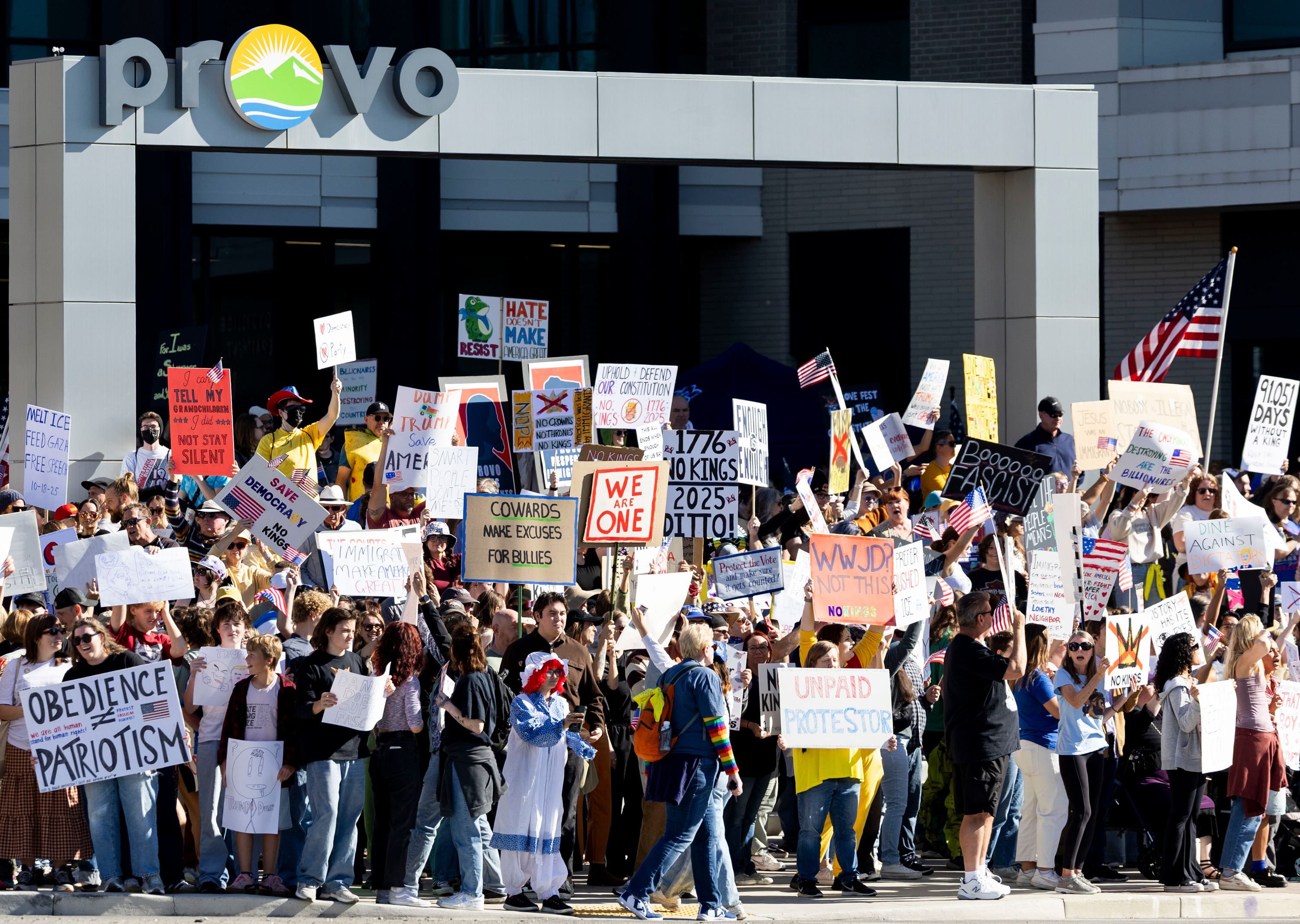 Protesters hold signs outside of City Hall in Provo for a “No Kings” protest on Saturday.