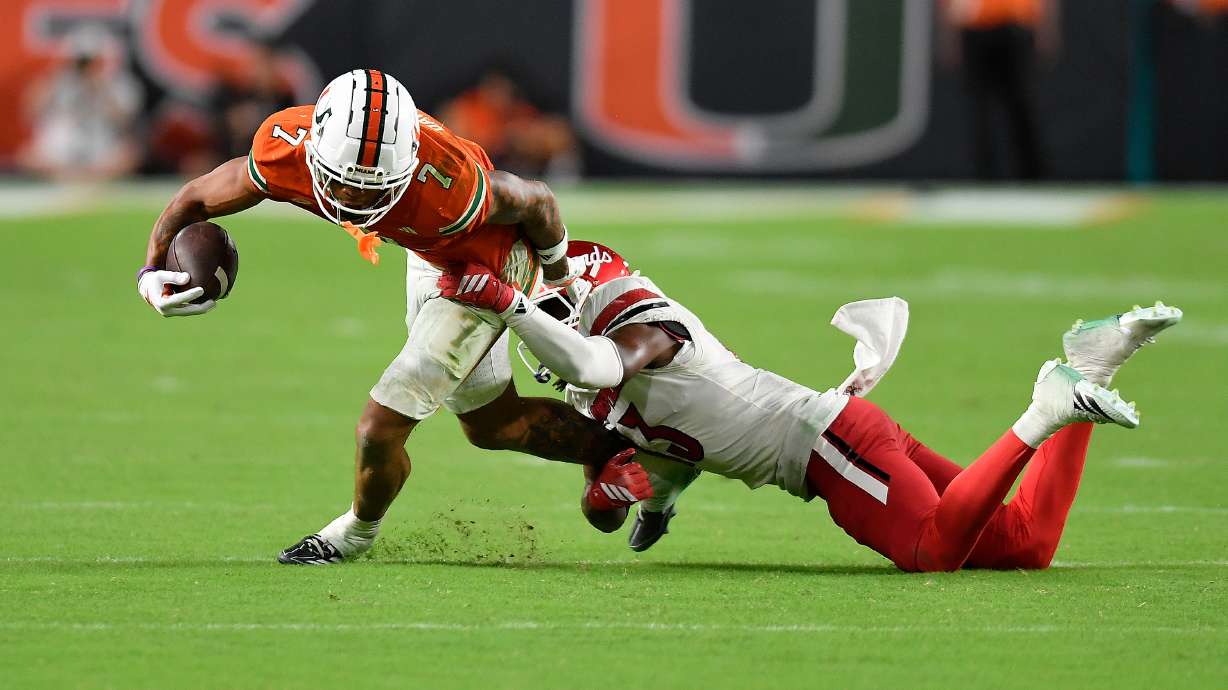 Miami wide receiver CJ Daniels (7) is tackled by Louisville cornerback Justin Agu during the second half of an NCAA college football game, Friday, Oct. 17, 2025, in Miami Gardens, Fla.