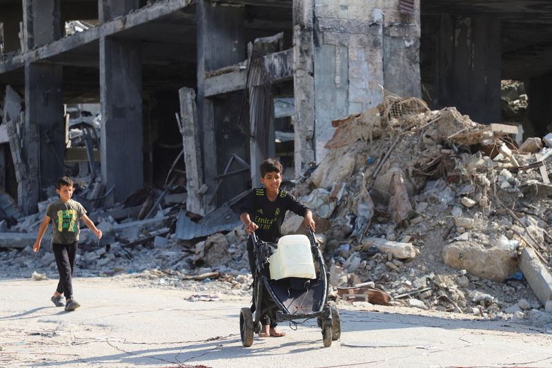 Displaced Palestinian children walk, as one of them moves a cart loaded with water containers, amid a ceasefire between Israel and Hamas, in Gaza City, Sunday.