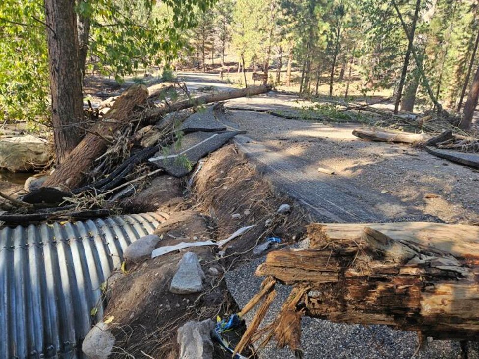 Road damage and debris from recent flash flooding over a water channel in Pine Valley.