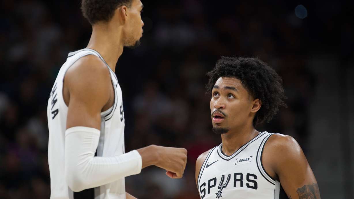 San Antonio Spurs center Victor Wembanyama, left, speaks with teammate Dylan Harper, right, during the first half of a preseason NBA basketball game against the Utah Jazz, Friday, Oct. 10, 2025, in San Antonio.