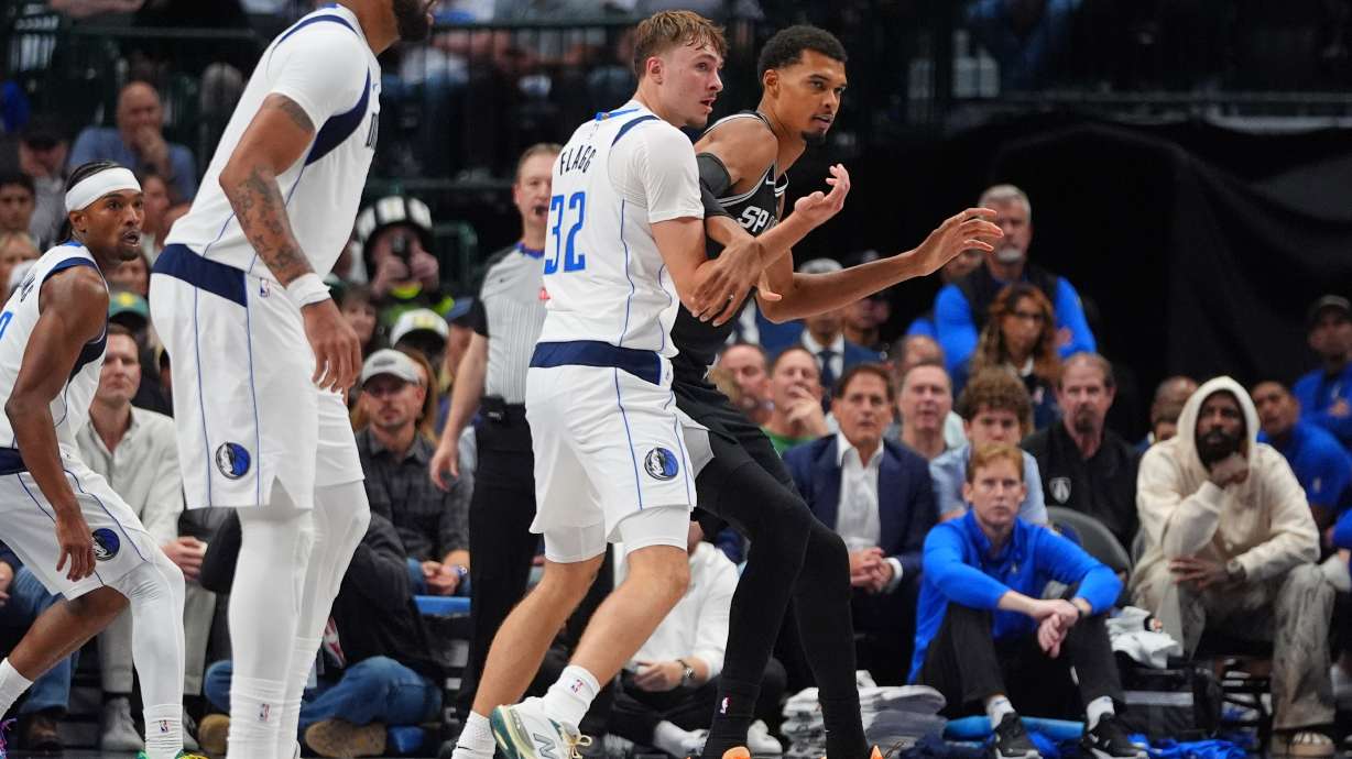 San Antonio Spurs forward Victor Wembanyama, right, is defended by Dallas Mavericks forward Cooper Flagg (32) as forward Anthony Davis, second from left, looks on during the second half of an NBA basketball game in Dallas, Wednesday, Oct. 22, 2025.