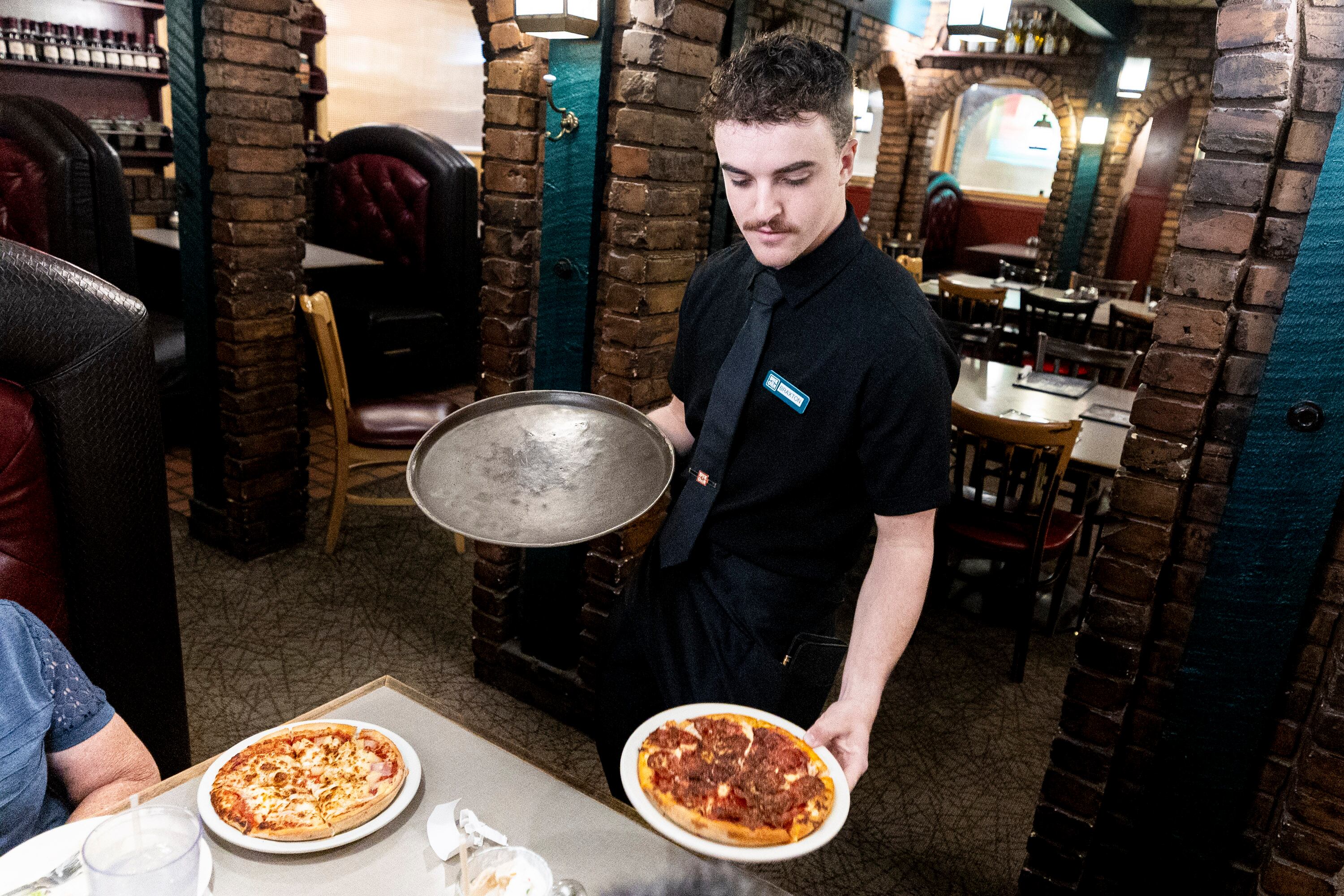 Braxton Brewer, a server at Brick Oven, serves pizza to customers at the restaurant in Provo on Friday.