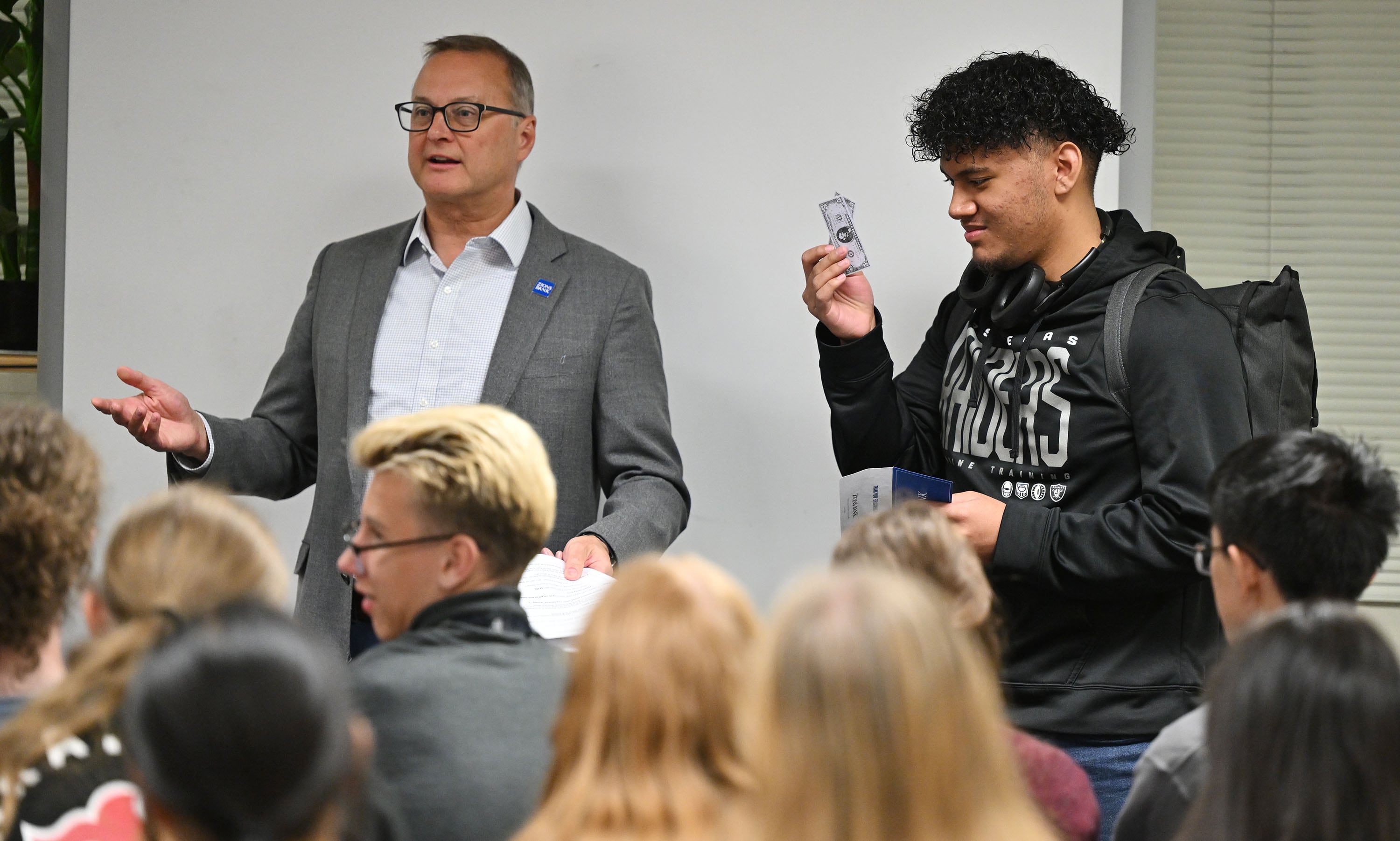 West High School student Penisimani Lafo holds up some play money as he helps Paul Burdiss, Zions Bank president and CEO, in a short demonstration on the practice of financial discipline being a key to avoiding snowballing debt in life, in Salt Lake City on Friday.