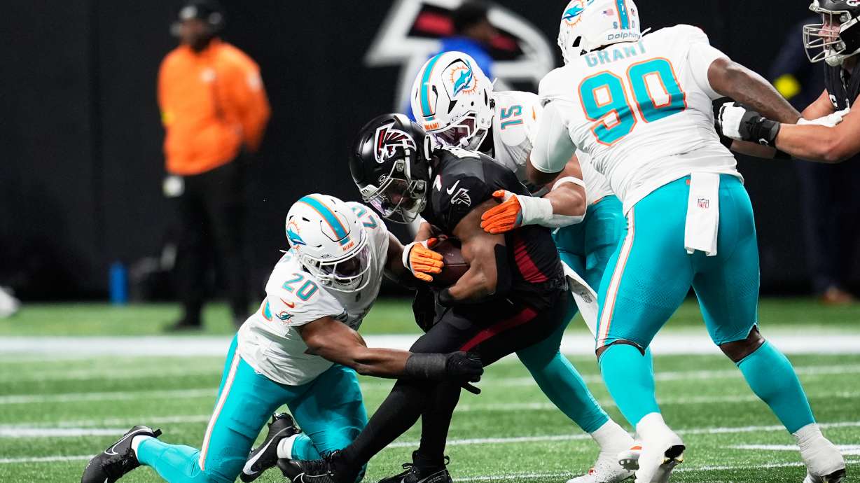 Miami Dolphins linebacker Jordyn Brooks (20) and linebacker Jaelan Phillips (15) defend Atlanta Falcons running back Bijan Robinson, center, during the first half of an NFL football game, Sunday, Oct. 26, 2025, in Atlanta.