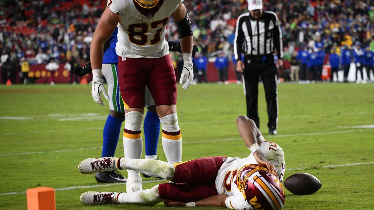 Washington Commanders tight end John Bates (87) looks over at his teammate quarterback Jayden Daniels (5) who injured his arm while being tackled by Seattle Seahawks linebacker Drake Thomas during the second half of an NFL football game, Sunday, Nov. 2, 2025, in Landover, Md.