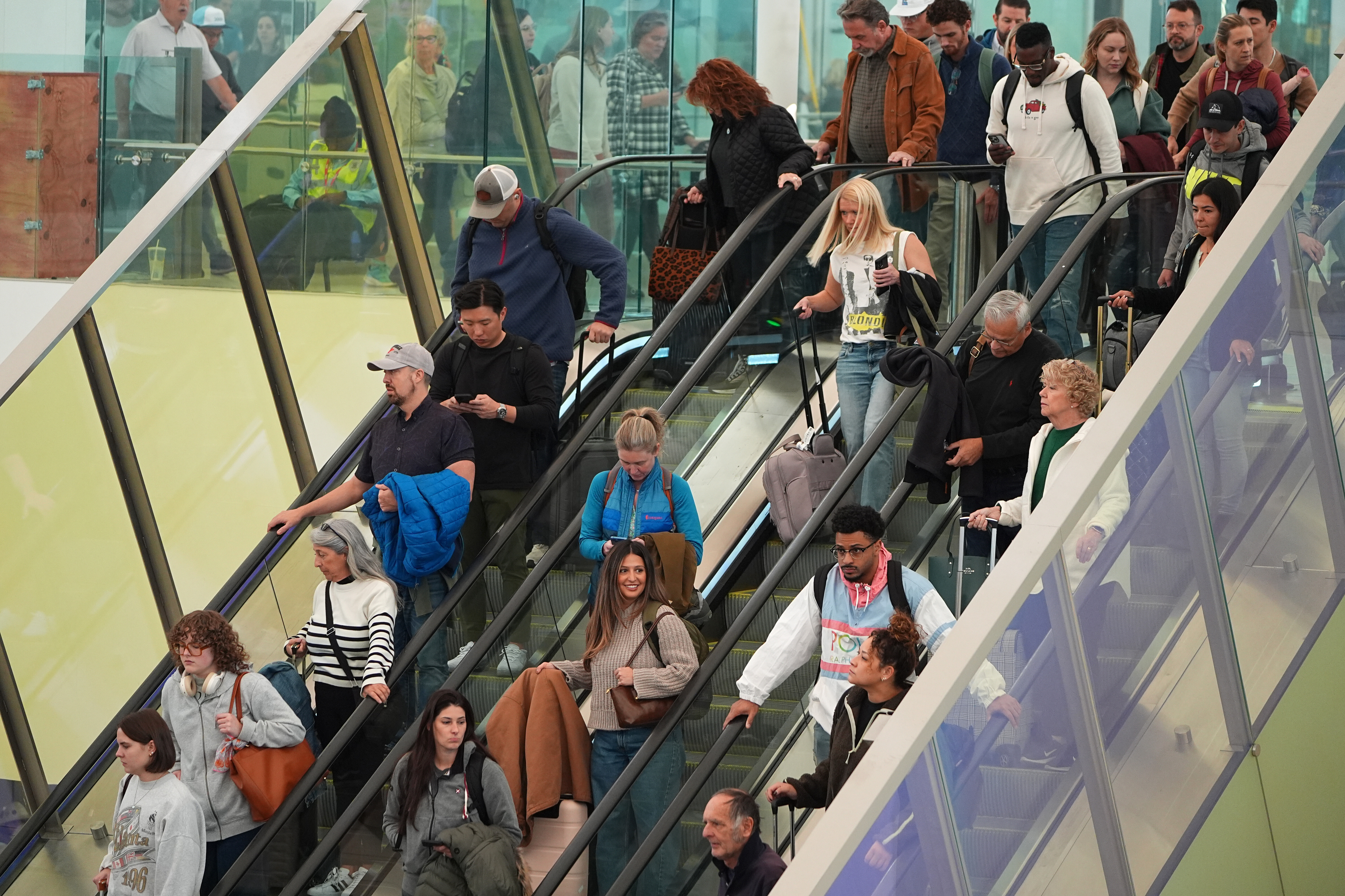 Travelers head down an escalator after clearing through a security checkpoint in Denver International Airport, Friday, in Denver. Some faced long lines at checkpoints while others pondered alternative travel options.