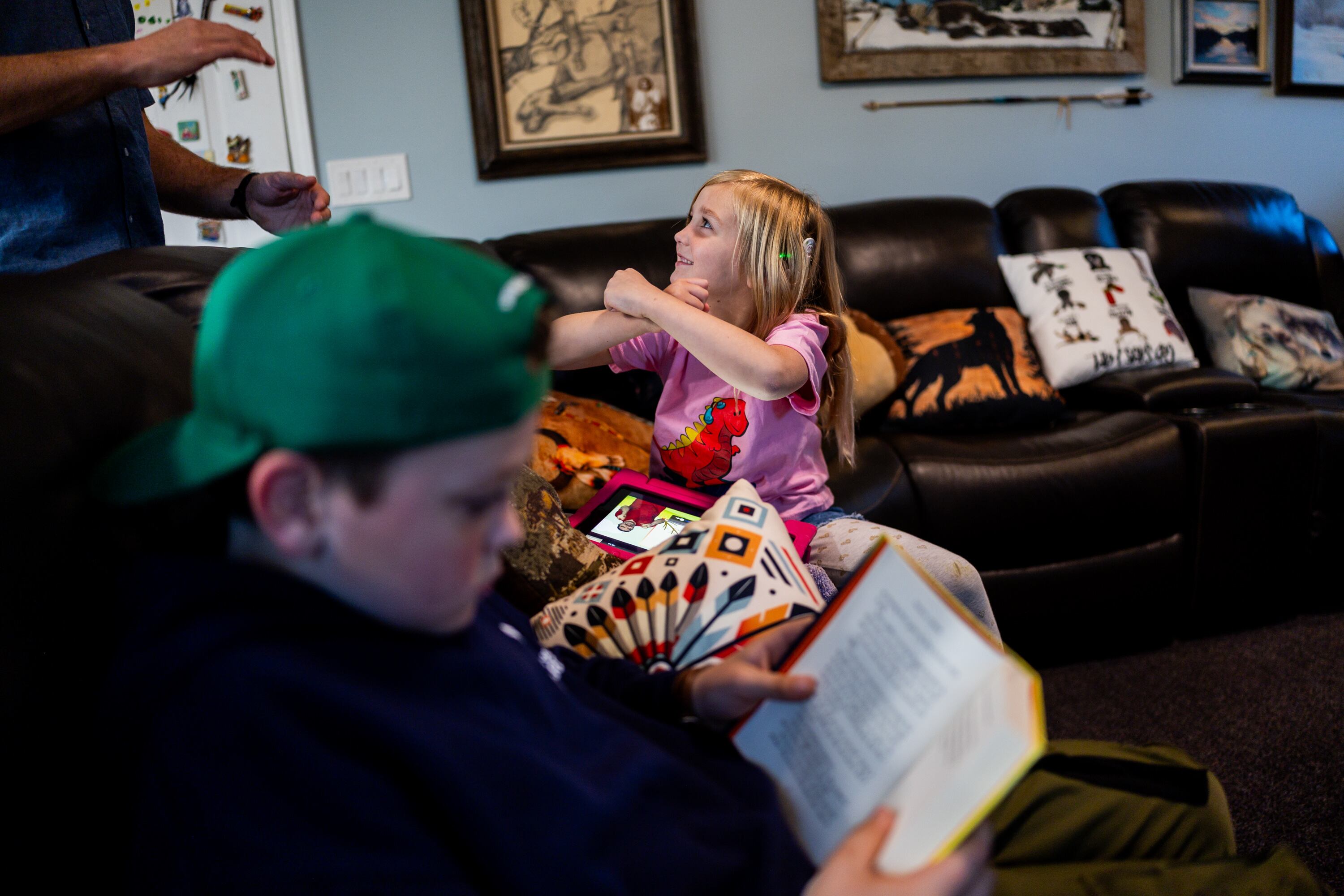 Philly Clancy, 5, center, a student at the Jean Massieu School of the Deaf, practices signing with her father Brian Clancy, back left, while her brother Boston Clancy, 8, a student at Majestic Elementary Arts Academy, left, reads a book at their home in South Jordan on Thursday. The Clancys say they're trying different things to strike the right balance.