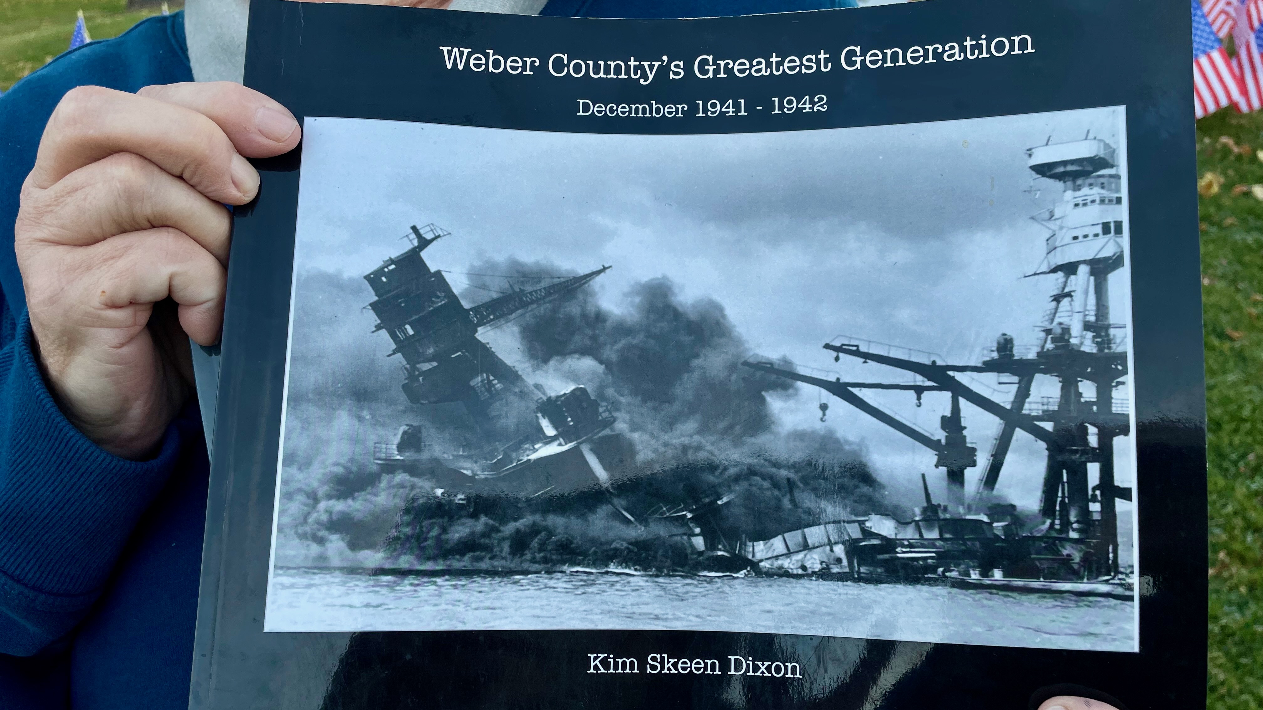 Kim Dixon, of West Haven, holds a copy of one of the books she compiled that outlines Weber County's role in World War II. She installed a field of 181 flags in an Ogden park on Tuesday to mark Veterans Day and honor the 181 Weber County service members killed in the war.