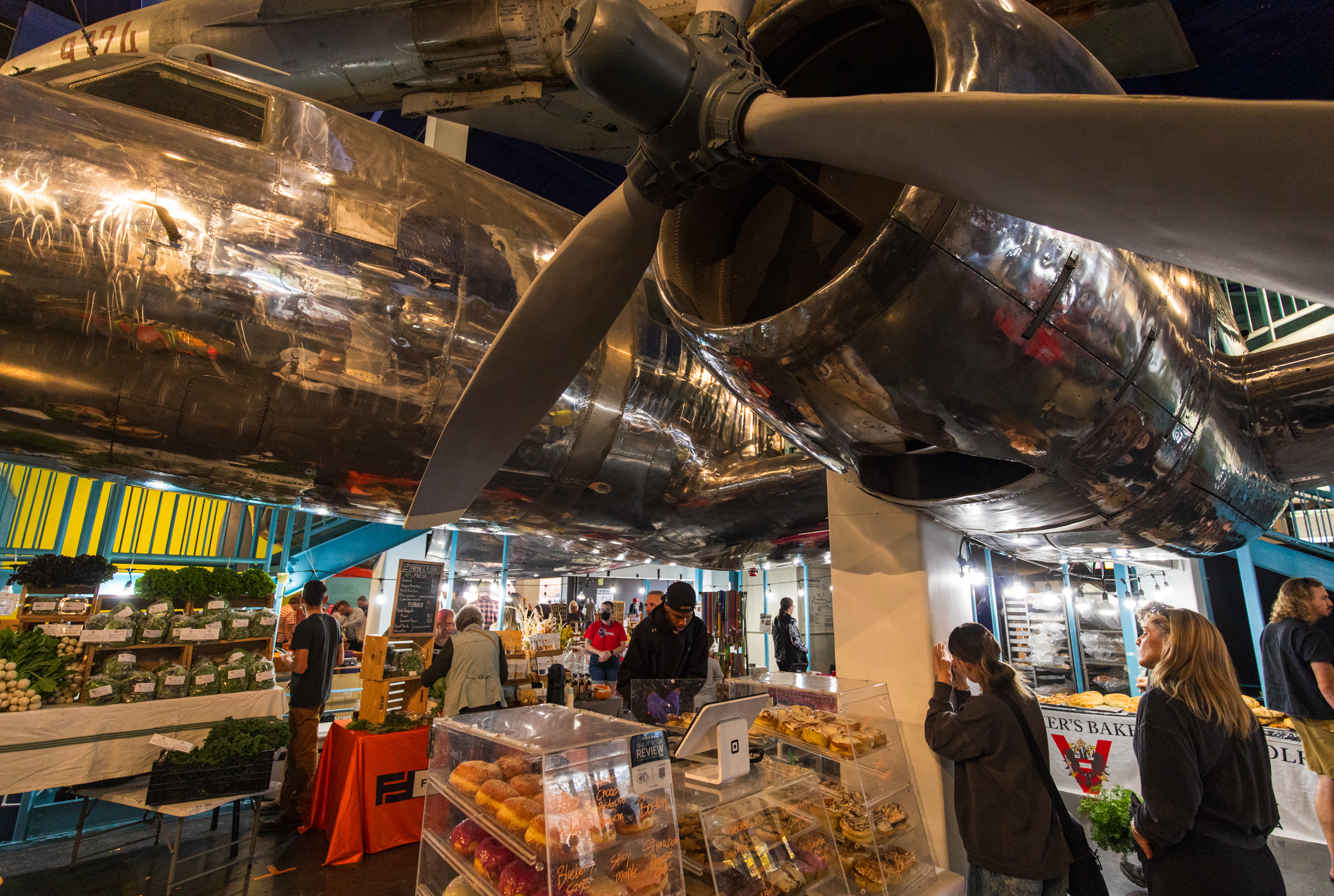Customers browse offerings at Eats Bakery, set up underneath a C-131 military transport plane at the Leonardo building in Salt Lake City on Saturday. Salt Lake City Downtown Farmers Market moved its winter market to the site this year.