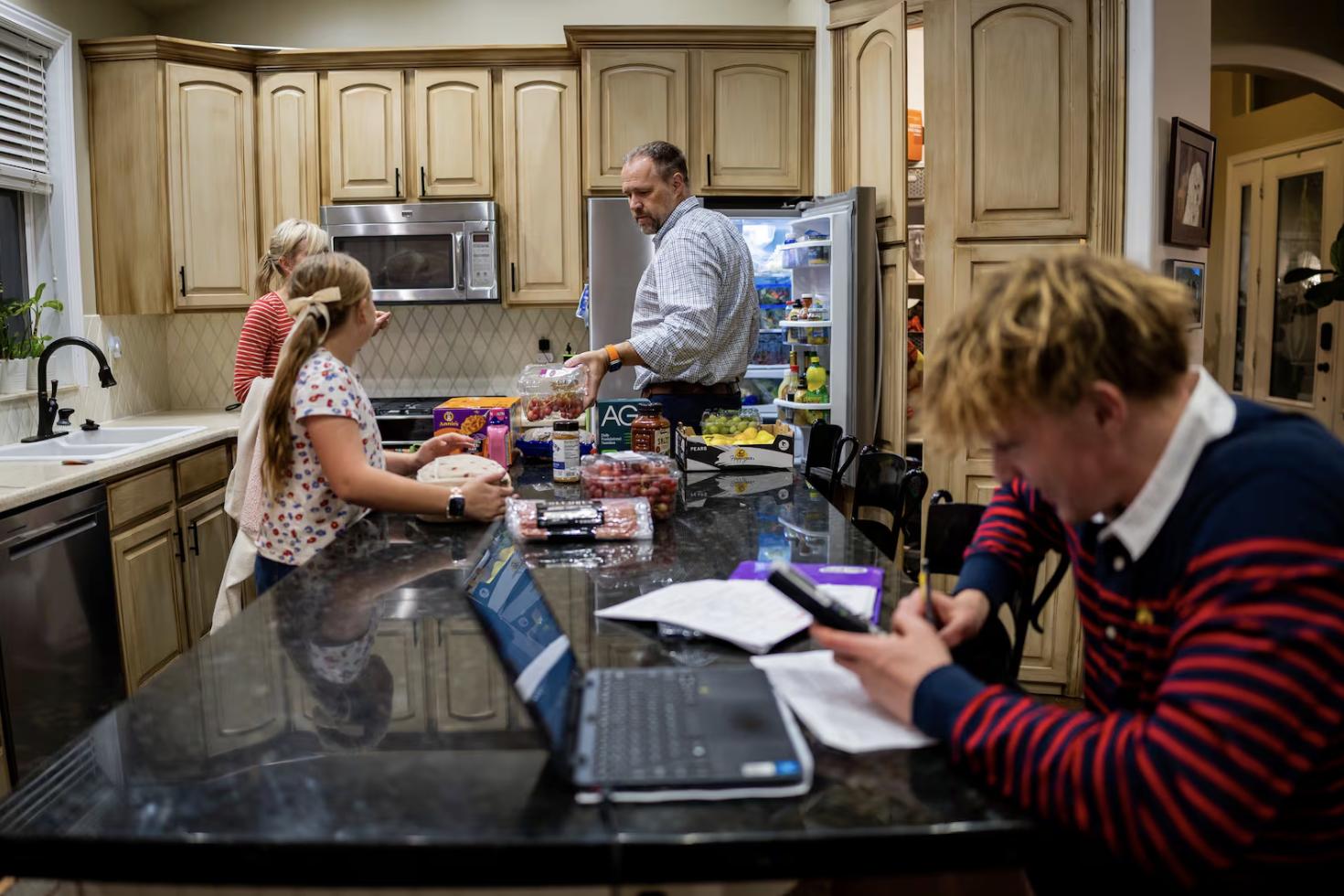 Jennifer Long, daughter Emily Long, 10, and husband Adam Long, from left, unload groceries while son Henry Long, 16, does his homework at their home in Bountiful on Nov. 6.