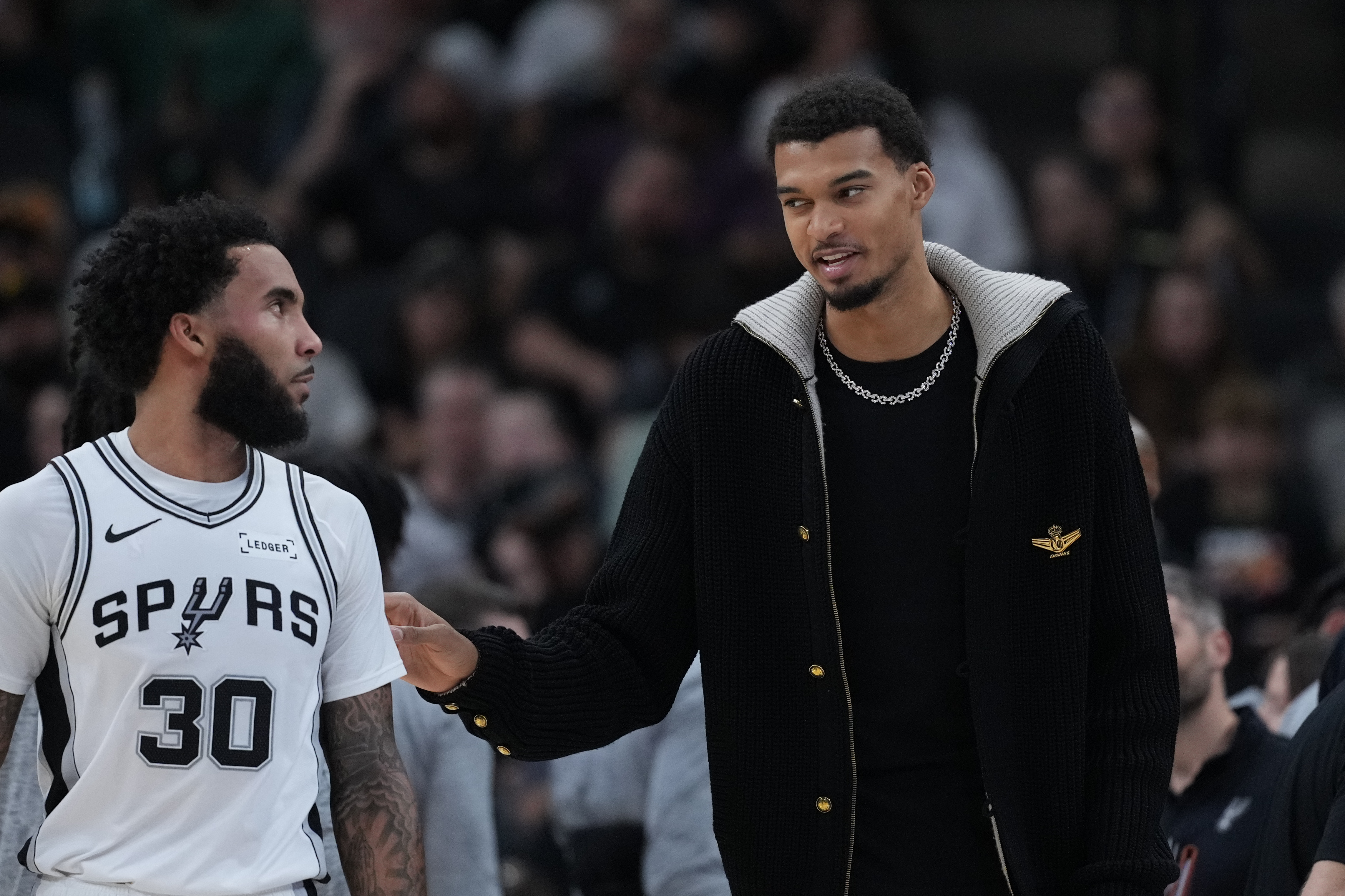 San Antonio Spurs forward Victor Wembanyama, right, talks with teamamte forward Julian Champagnie (30) during the first half of an NBA basketball game against the Sacramento Kings in San Antonio, Sunday, Nov. 16, 2025.