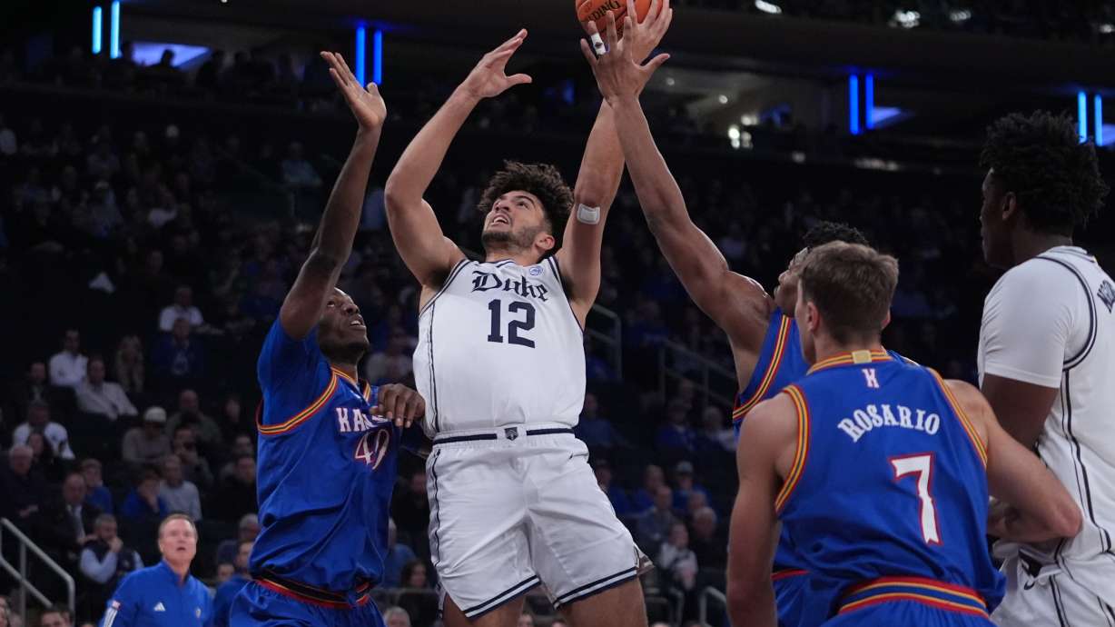 Duke's Cameron Boozer (12) drives past Kansas' Flory Bidunga (40) and Kohl Rosario (7) during the first half of an NCAA college basketball game Tuesday, Nov. 18, 2025, in New York.