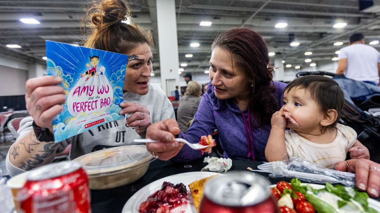 Treena Vigil shows Danielle Cameron and her daughter Xochitl Gonzales a free book at the Larry H. Miller Company and the Miller family’s 26th Annual Season of Service Thanksgiving Meal and Community Resource Event at the Salt Palace Convention Center in Salt Lake City on Nov. 25, 2024.