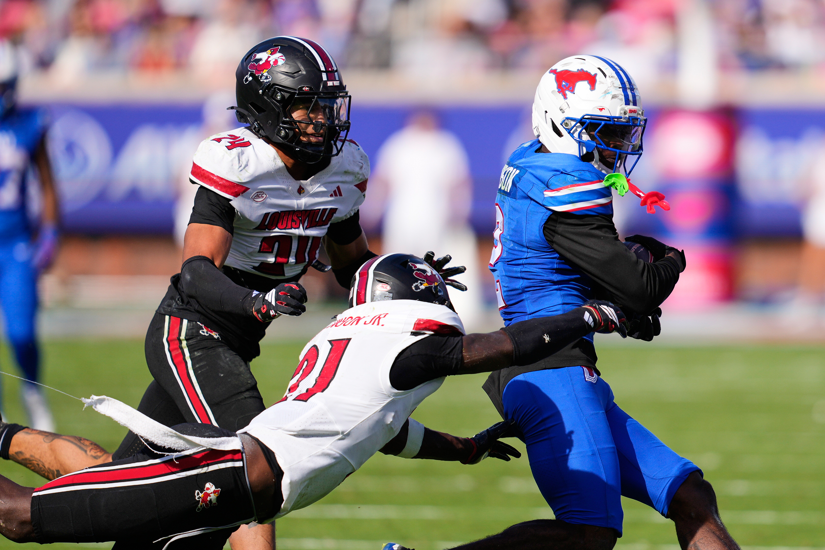 SMU wide receiver Jordan Hudson (2) catches a pass and is tackled by Louisville defensive back D'Angelo Hutchinson (21) and defensive back Corey Gordon (24) in the second half of an NCAA college football game Saturday, Nov. 22, 2025, in Dallas. 