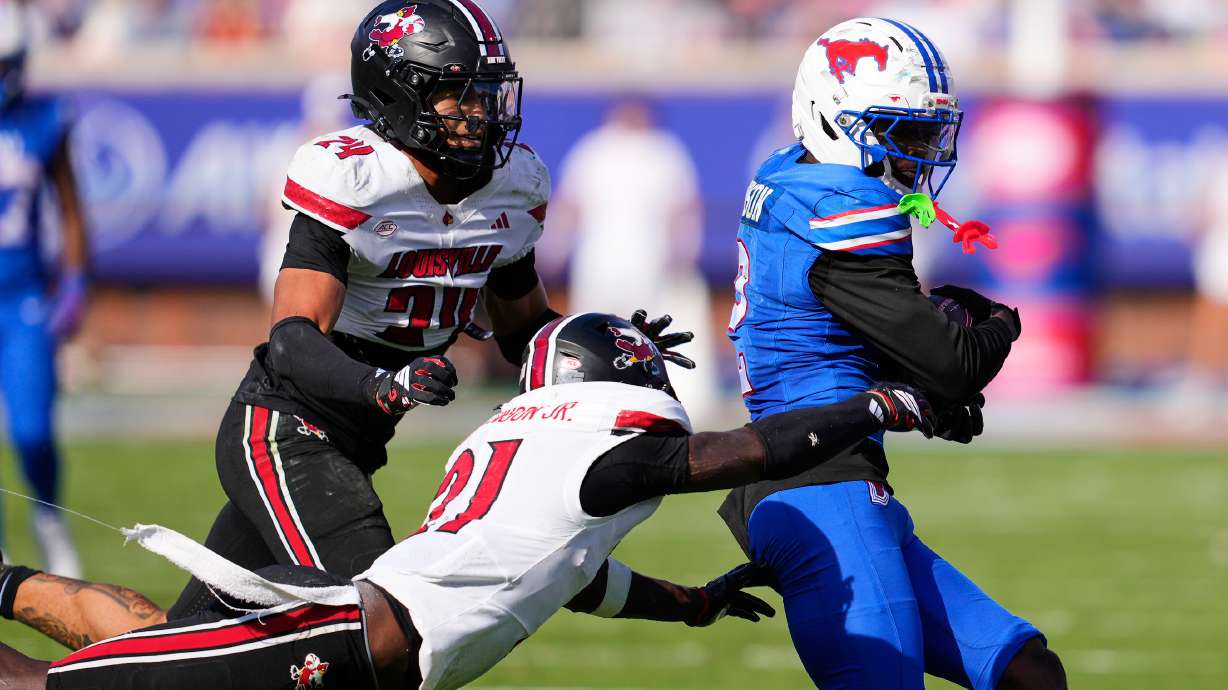 SMU wide receiver Jordan Hudson (2) catches a pass and is tackled by Louisville defensive back D'Angelo Hutchinson (21) and defensive back Corey Gordon (24) in the second half of an NCAA college football game Saturday, Nov. 22, 2025, in Dallas.