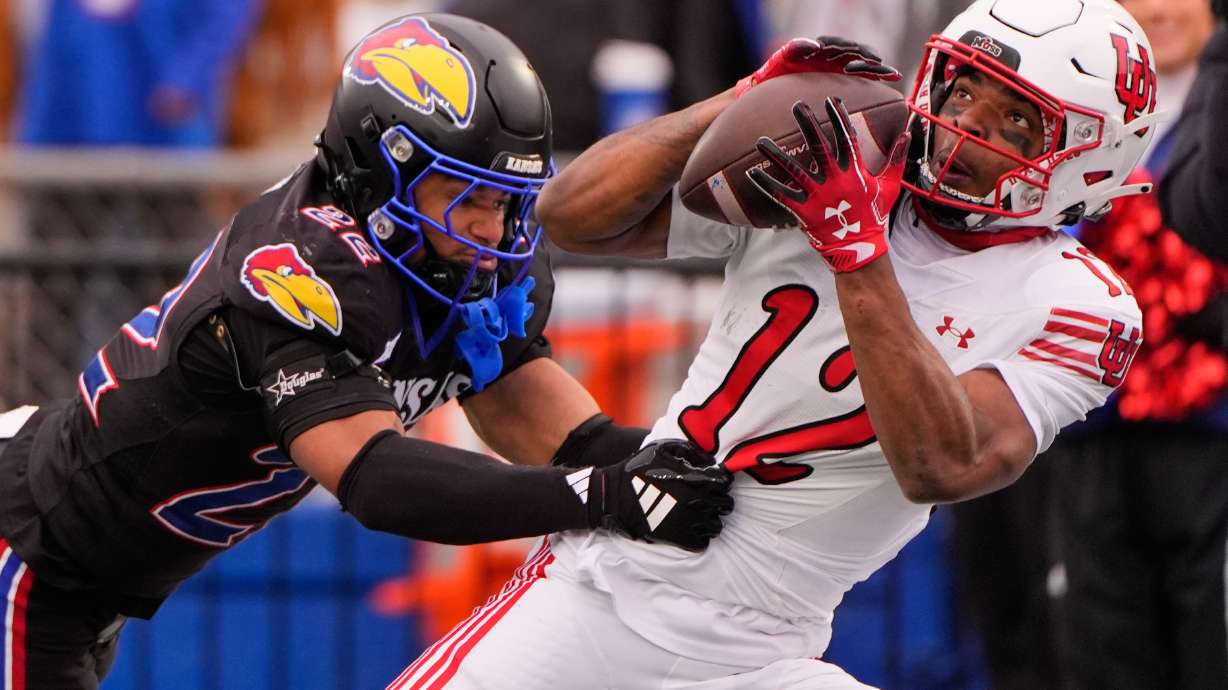 Utah wide receiver Larry Simmons (12) catches a pass under pressure from Kansas defensive back Syeed Gibbs (22) to score a touchdown during the second half of an NCAA college football game Friday, Nov. 28, 2025, in Lawrence, Kan.