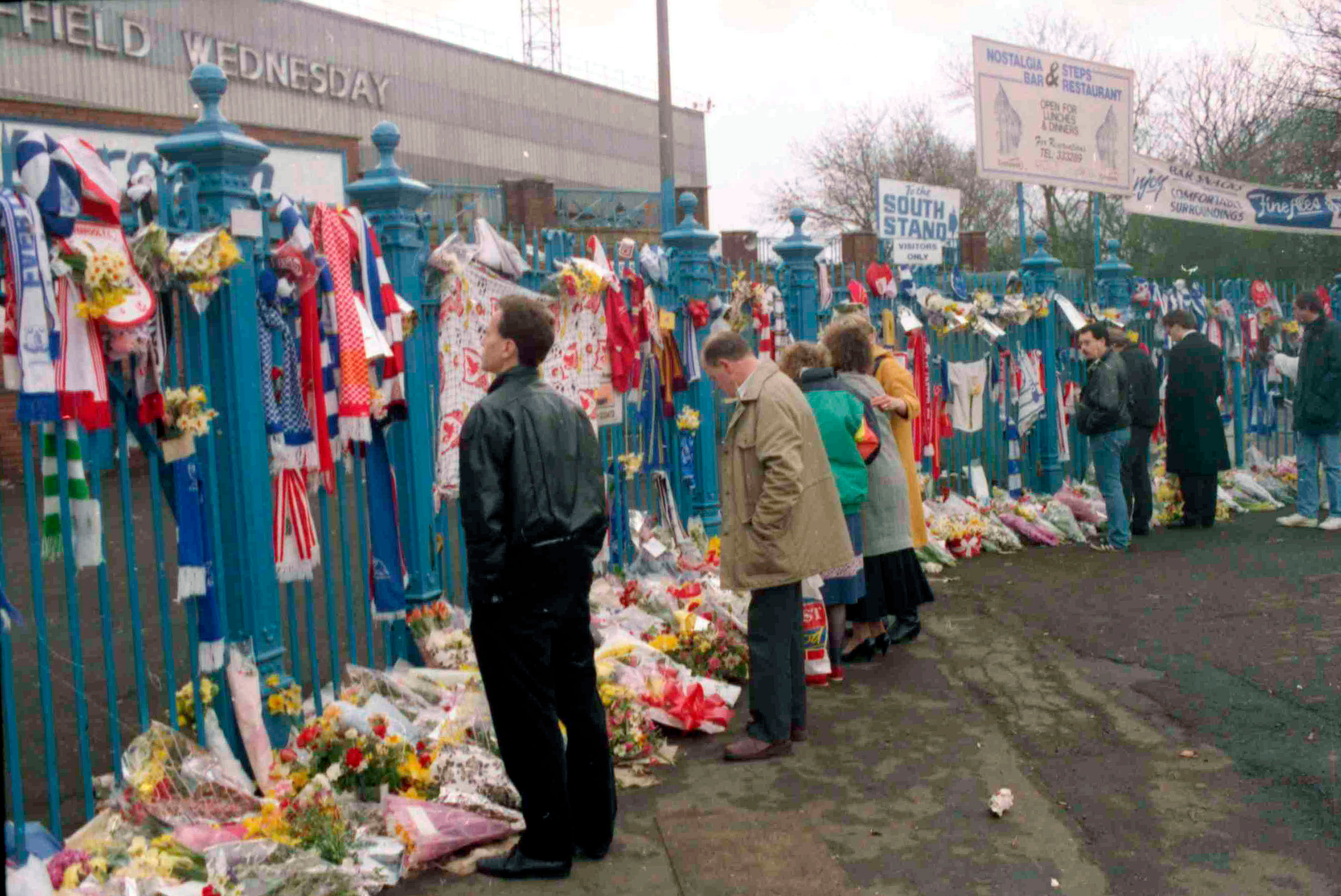 FILE- In this file photo dated April 17, 1989, soccer fans arrive to pay their respects and look at the flowers, scarves and banners, left on the gates at Hillsborough Football Stadium. 