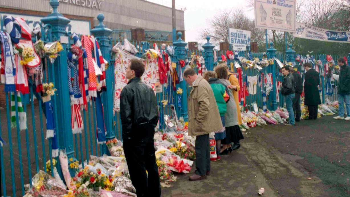 FILE- In this file photo dated April 17, 1989, soccer fans arrive to pay their respects and look at the flowers, scarves and banners, left on the gates at Hillsborough Football Stadium.