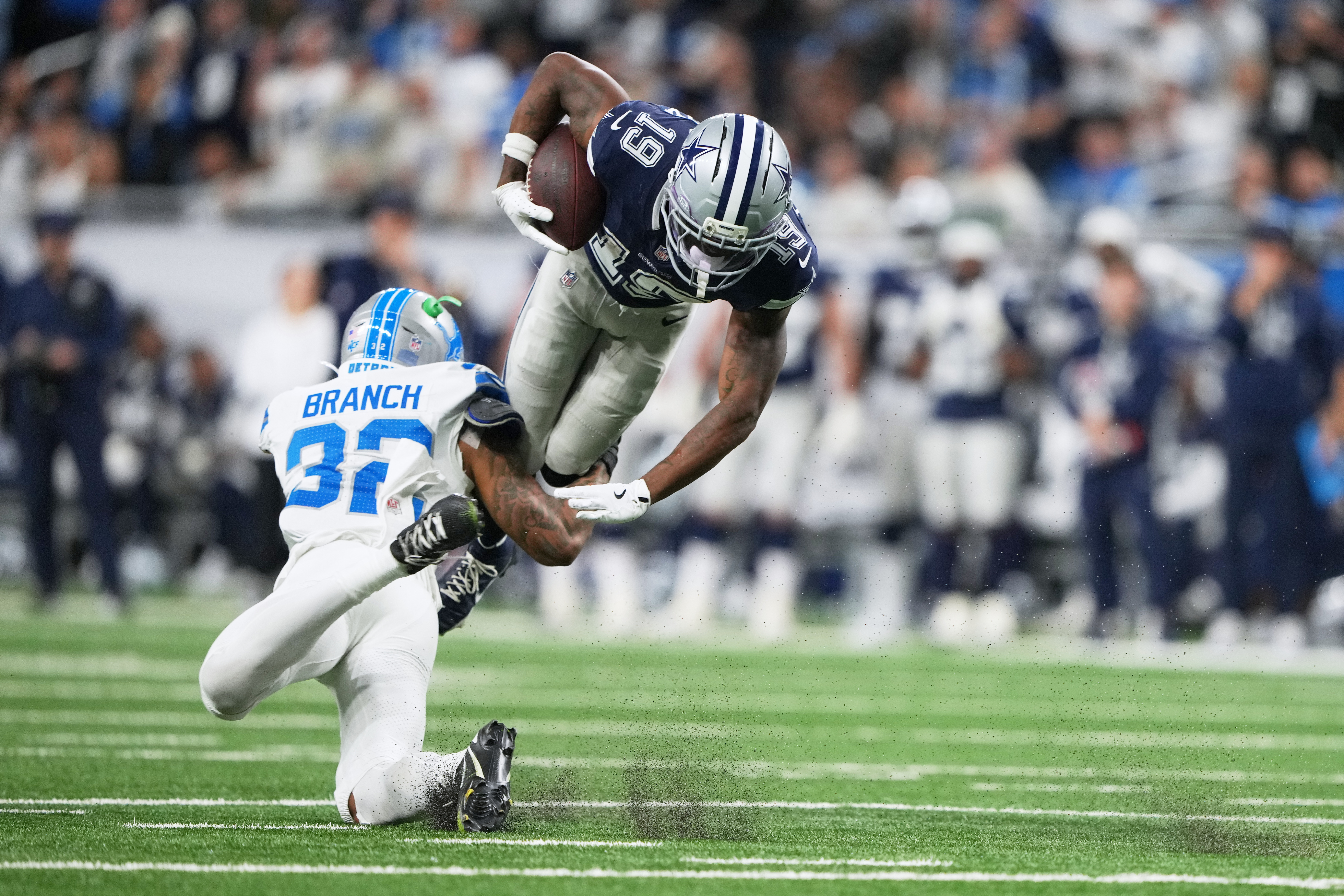 Dallas Cowboys wide receiver Ryan Flournoy (19) takes a hit from Detroit Lions safety Brian Branch (32) during the second half of an NFL football game Thursday, Dec. 4, 2025, in Detroit.