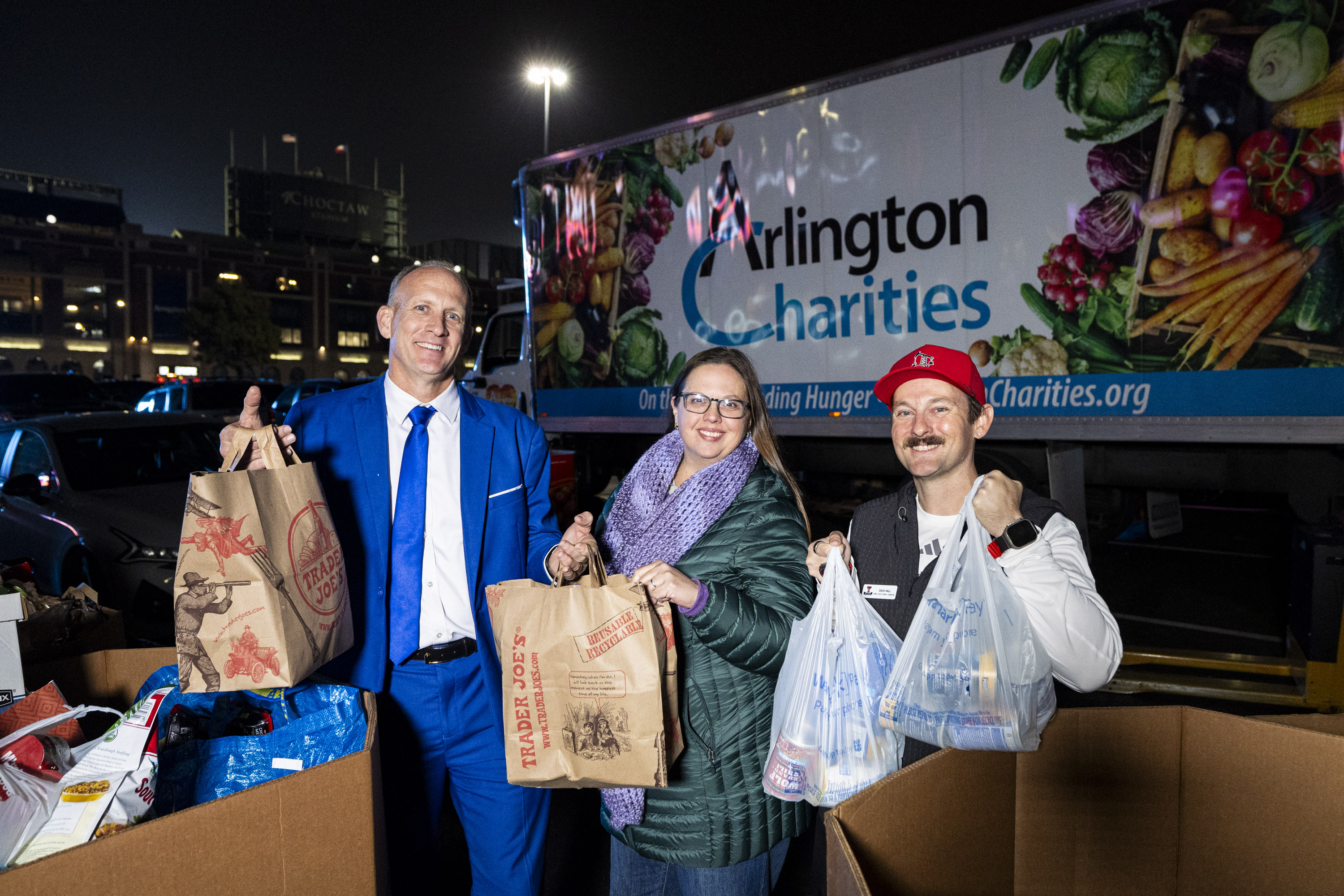 From left, Taggart Barron, chapter chair of the Texas - Dallas/Forth Worth BYU Alumni Chapter, Heather Lowe, development director of Arlington Charities, and Zach Hall, chapter president of the Dallas County Texas Tech Alumni Chapter, pose together for a photo as part of a food drive with Arlington Charities during pregame festivities for BYU fans held the day before the Big 12 championship game at Globe Life Field in Arlington, Texas, on Friday, Dec. 5, 2025.