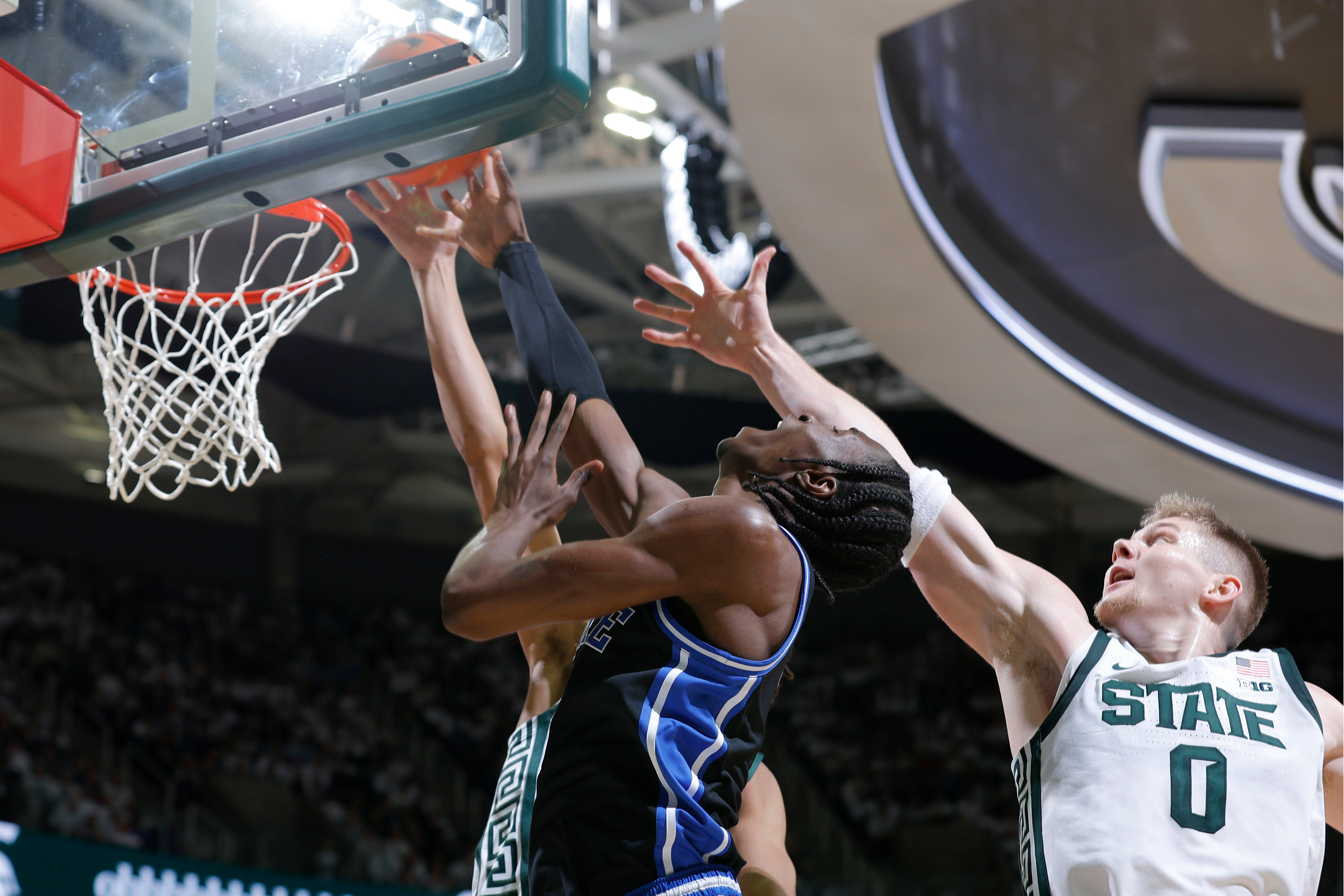 Duke guard Dame Sarr, center, and Michigan State forward Jaxon Kohler (0), right, and forward Jordan Scott, rear, vie for a rebound during the first half of an NCAA college basketball game, Saturday, Dec. 6, 2025, in East Lansing, Mich. 