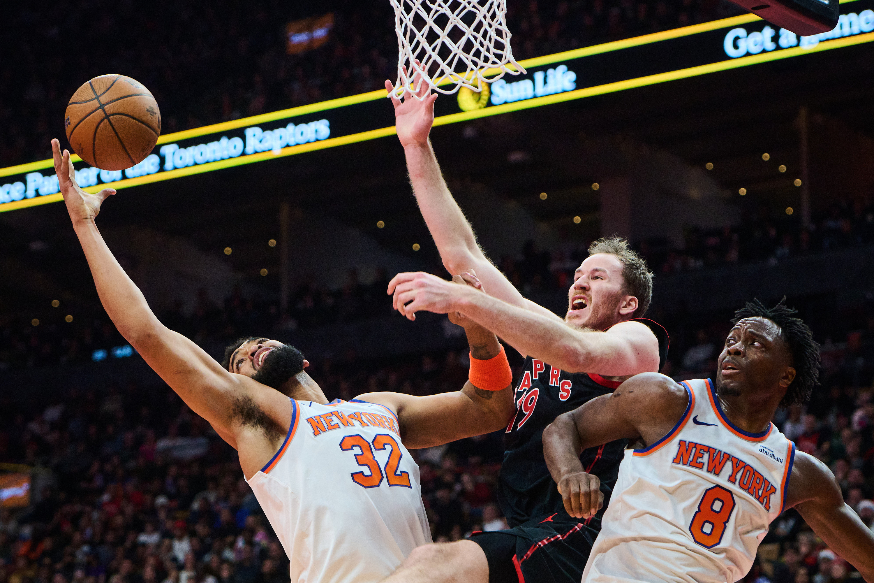 Toronto Raptors' Jakob Poeltl (19) is stopped at the net by New York Knicks' Karl-Anthony Towns (32) and New York Knicks' OG Anunoby (8) during the first half of an NBA Cup basketball game in Toronto, Tuesday, Dec. 9, 2025. 