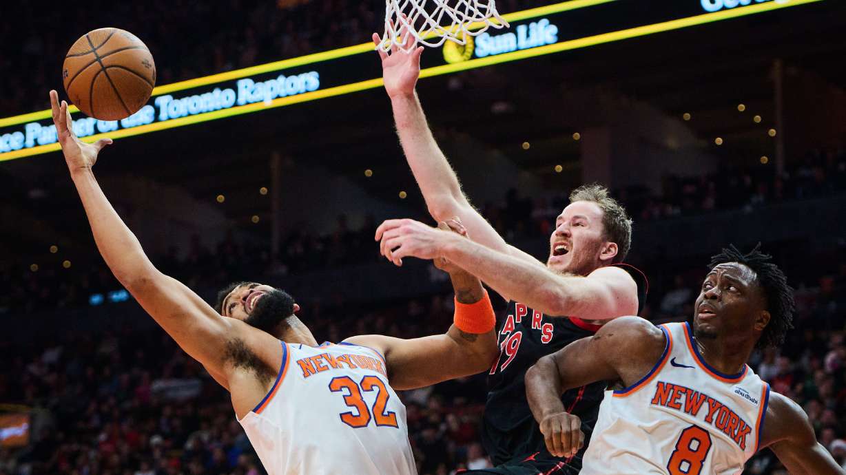 Toronto Raptors' Jakob Poeltl (19) is stopped at the net by New York Knicks' Karl-Anthony Towns (32) and New York Knicks' OG Anunoby (8) during the first half of an NBA Cup basketball game in Toronto, Tuesday, Dec. 9, 2025.