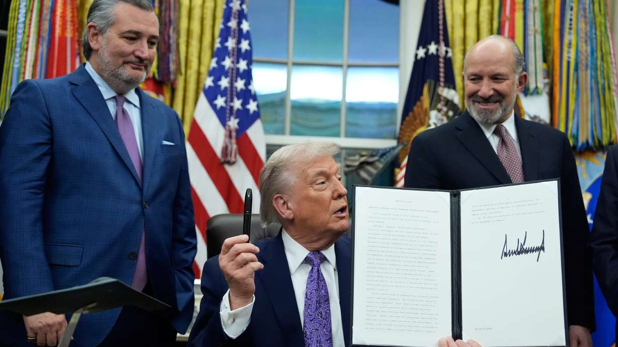 Flanked by Sen. Ted Cruz R-Texas, left, and Secretary of Commerce Howard Lutnick, President Donald Trump displays his signed AI initiative in the Oval Office of the White House, Thursday, in Washington.