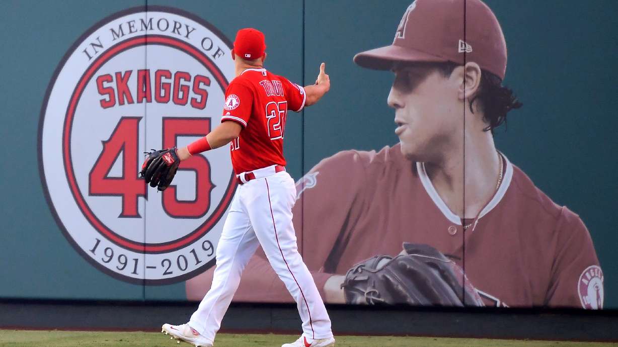 FILE - Los Angeles Angels center fielder Mike Trout gestures toward a photo of Tyler Skaggs in center field prior to a baseball game against the Detroit Tigers in Anaheim, Calif., on July 29, 2019.