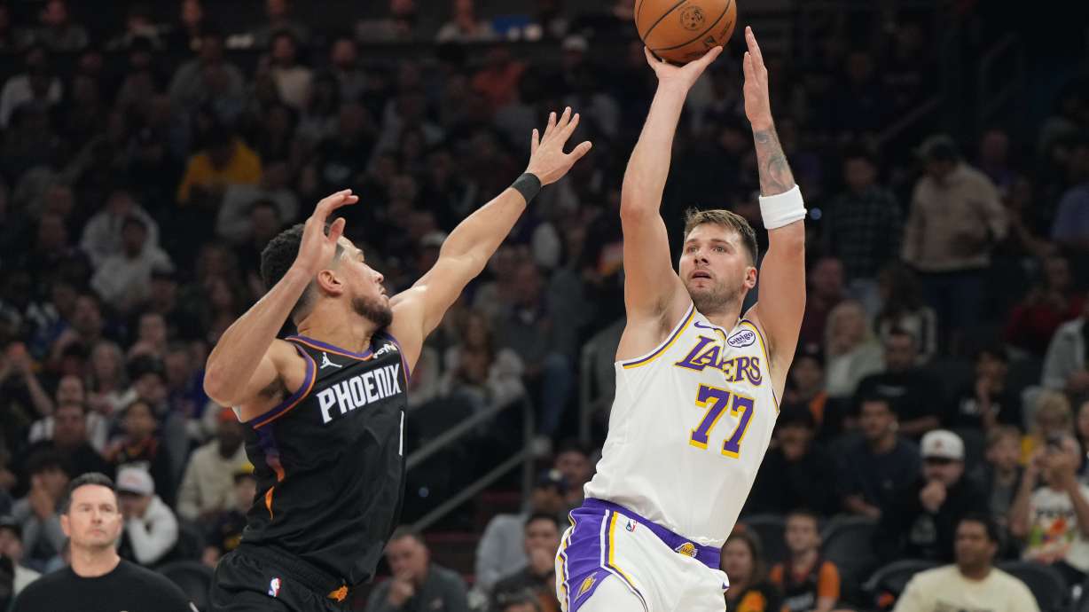 Los Angeles Lakers guard Luka Doncic (77)looks to shoot over Phoenix Suns guard Devin Booker, front left, during the first half of an NBA basketball game, Sunday, Dec. 14, 2025, in Phoenix.