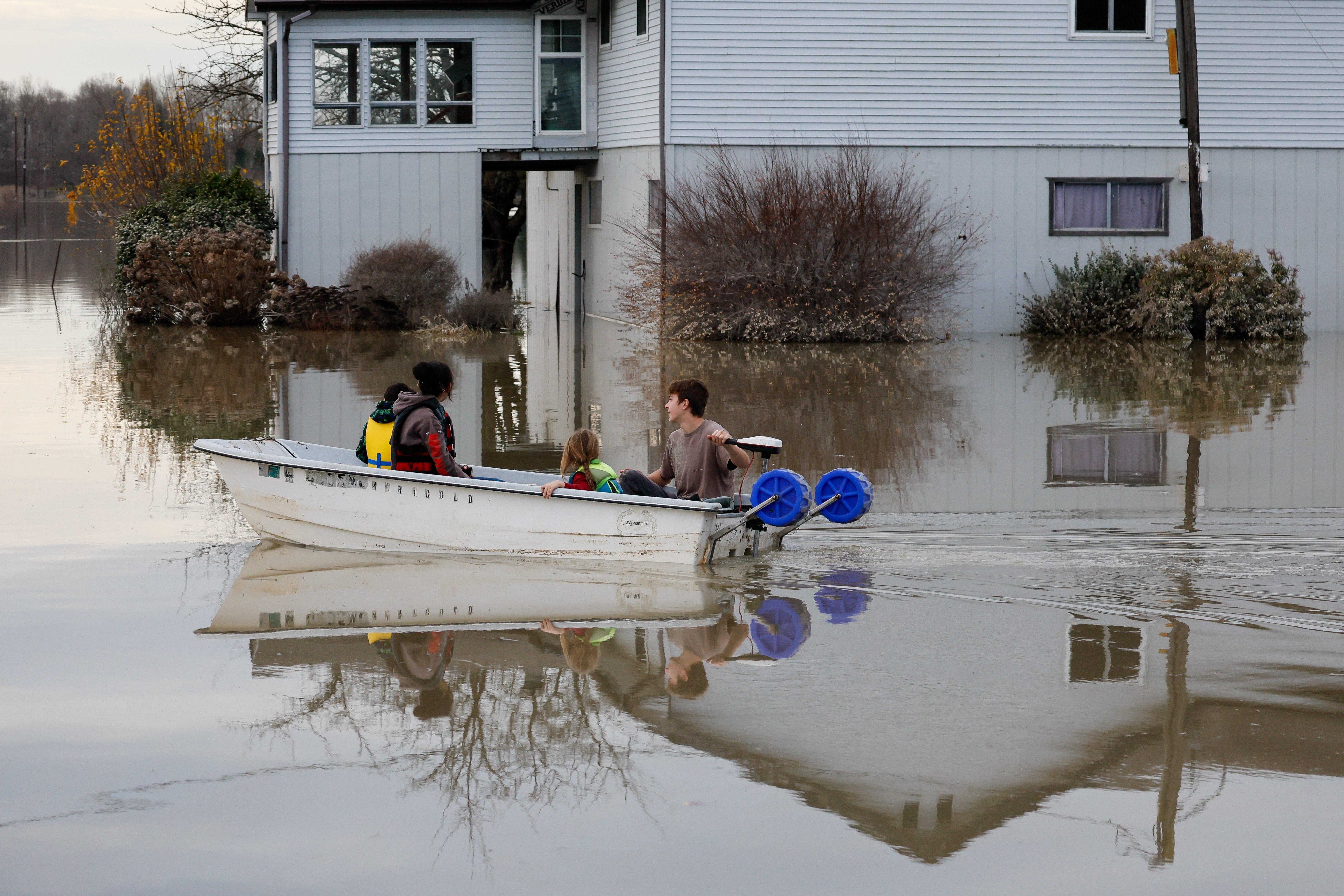 Carter Johnson, 16, uses a boat to transport his 5-year-old brother, Milo, and two neighbors past a flooded house in what was their front yard Saturday, near Clear Lake, Wash.
