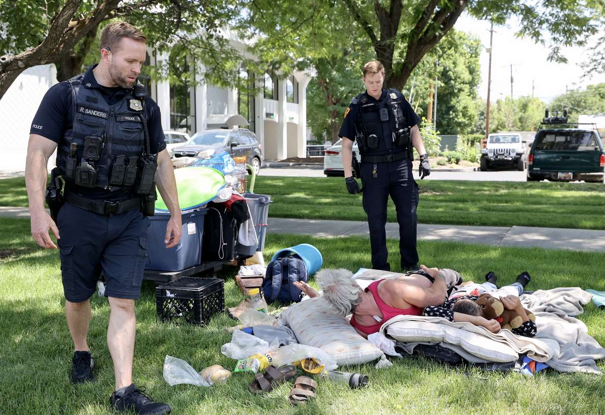 Salt Lake City Police Sgt. Ryan Sanders, who oversees the homeless resource center squad, and Salt Lake City Police officer Kent Krzymowski speak with two people experiencing homeless about camping laws in Salt Lake City on July 16, 2025.