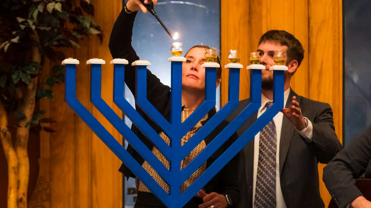 Rabbi Samuel Spector, of Congregation Kol Ami in Salt Lake City, right, assists Salt Lake City Mayor Erin Mendenhall, left, in lighting a menorah during a ceremony at the Salt Lake City-County Building in Salt Lake City on Wednesday.