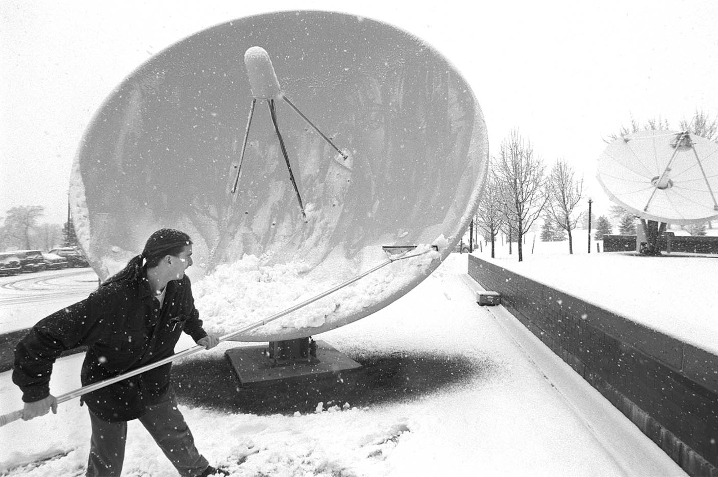James Hodges, 25, a television engineer at the Dolores Eccles Broadcasting Center, cleans off the satellite dishes Feb. 24, 1998, during a snowstorm.