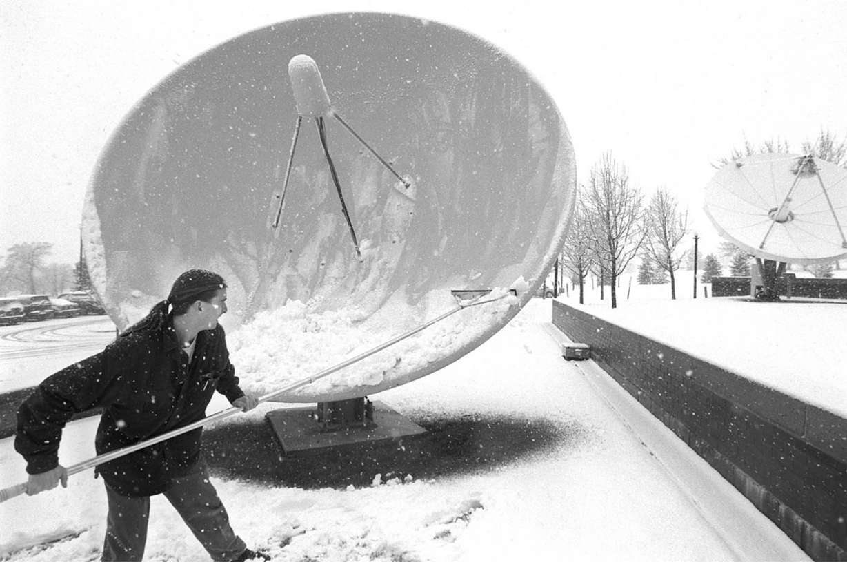 James Hodges, 25, a television engineer at the Dolores Eccles Broadcasting Center, cleans off the satellite dishes Feb. 24, 1998, during a snowstorm.