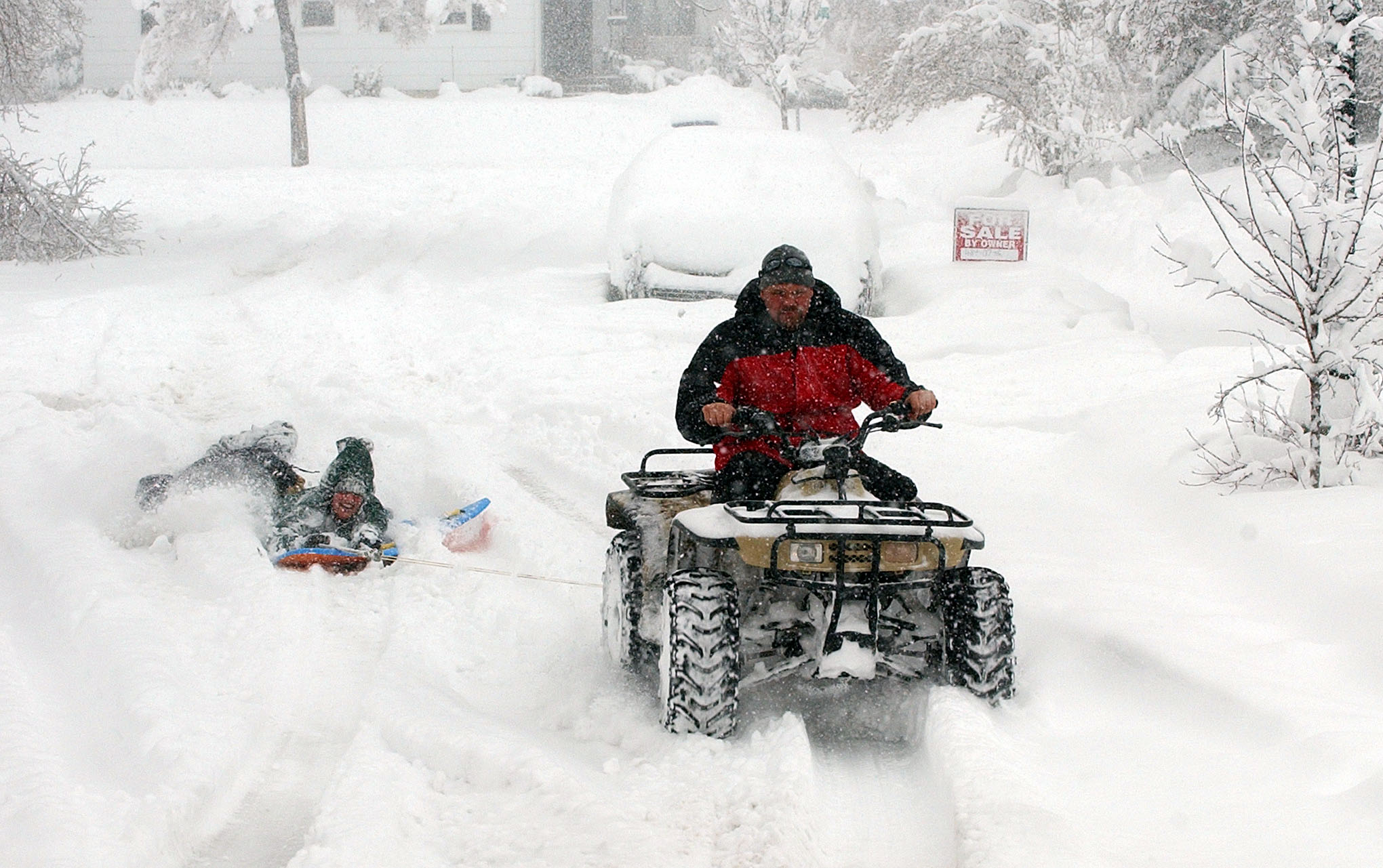 Jim Keech drives a four-wheeler pulling Robin Sumsion and Marin Keech on Claybourne Avenue in Salt Lake City during a snowstorm. Jim said this is the first time he has been able to do this since 1993.