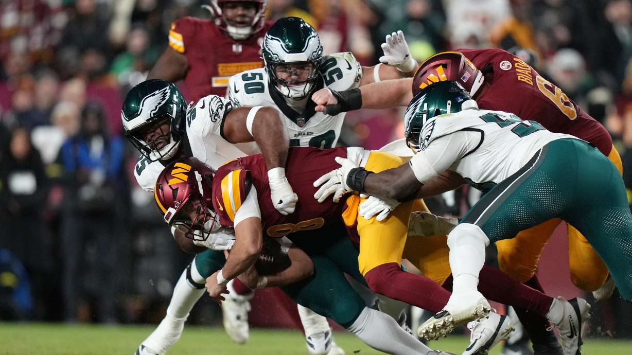 Washington Commanders quarterback Marcus Mariota (8) is sacked by Philadelphia Eagles defensive end Brandon Graham (55) during the first half of an NFL football game, Saturday, Dec. 20, 2025, in Landover, Md.