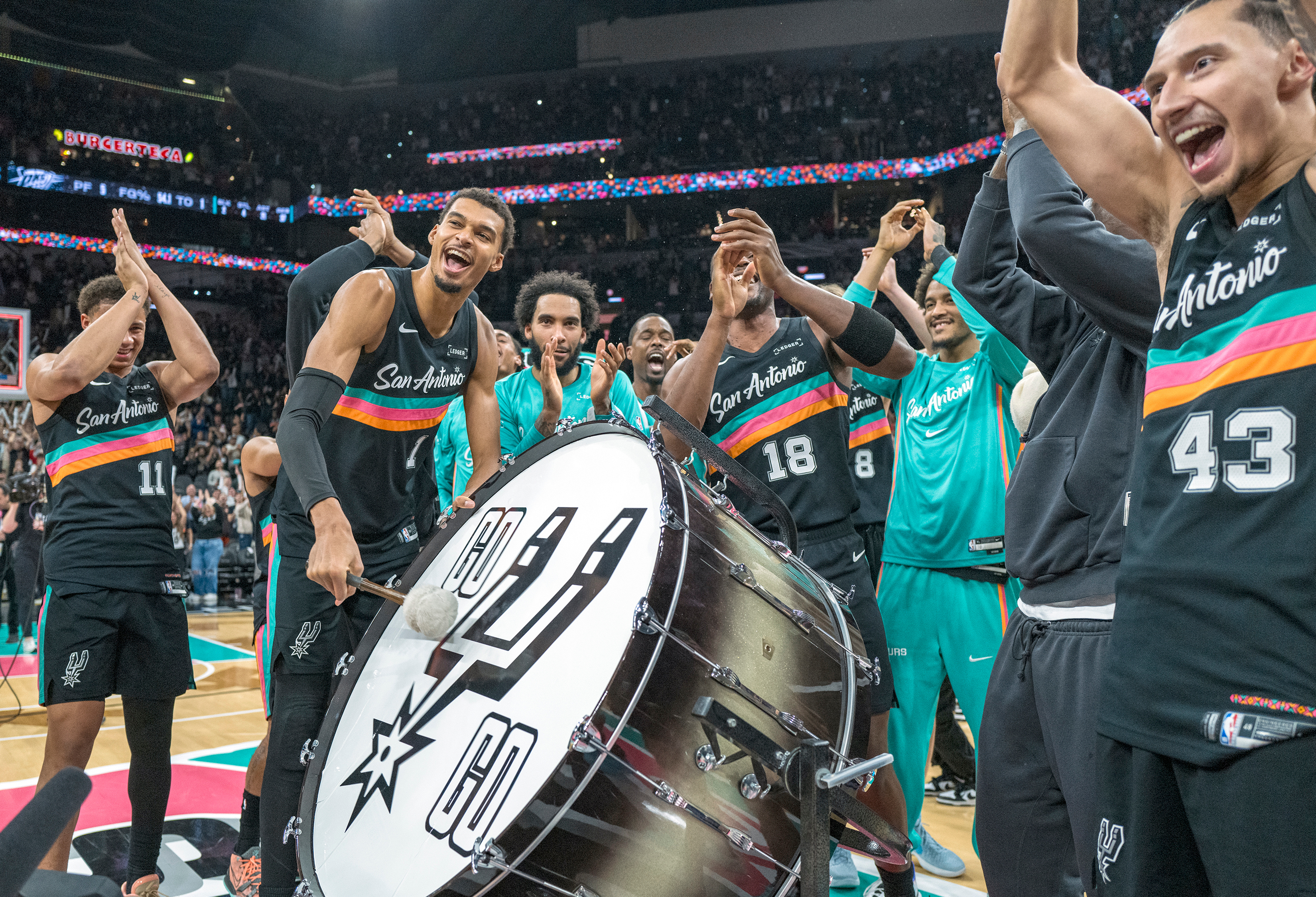 San Antonio Spurs forward Victor Wembanyama (1) hits on a drum as he and teammates celebrate with the Spurs fans after defeating the Oklahoma Thunder in an NBA basketball game in San Antonio, Tuesday, Dec. 23, 2025.