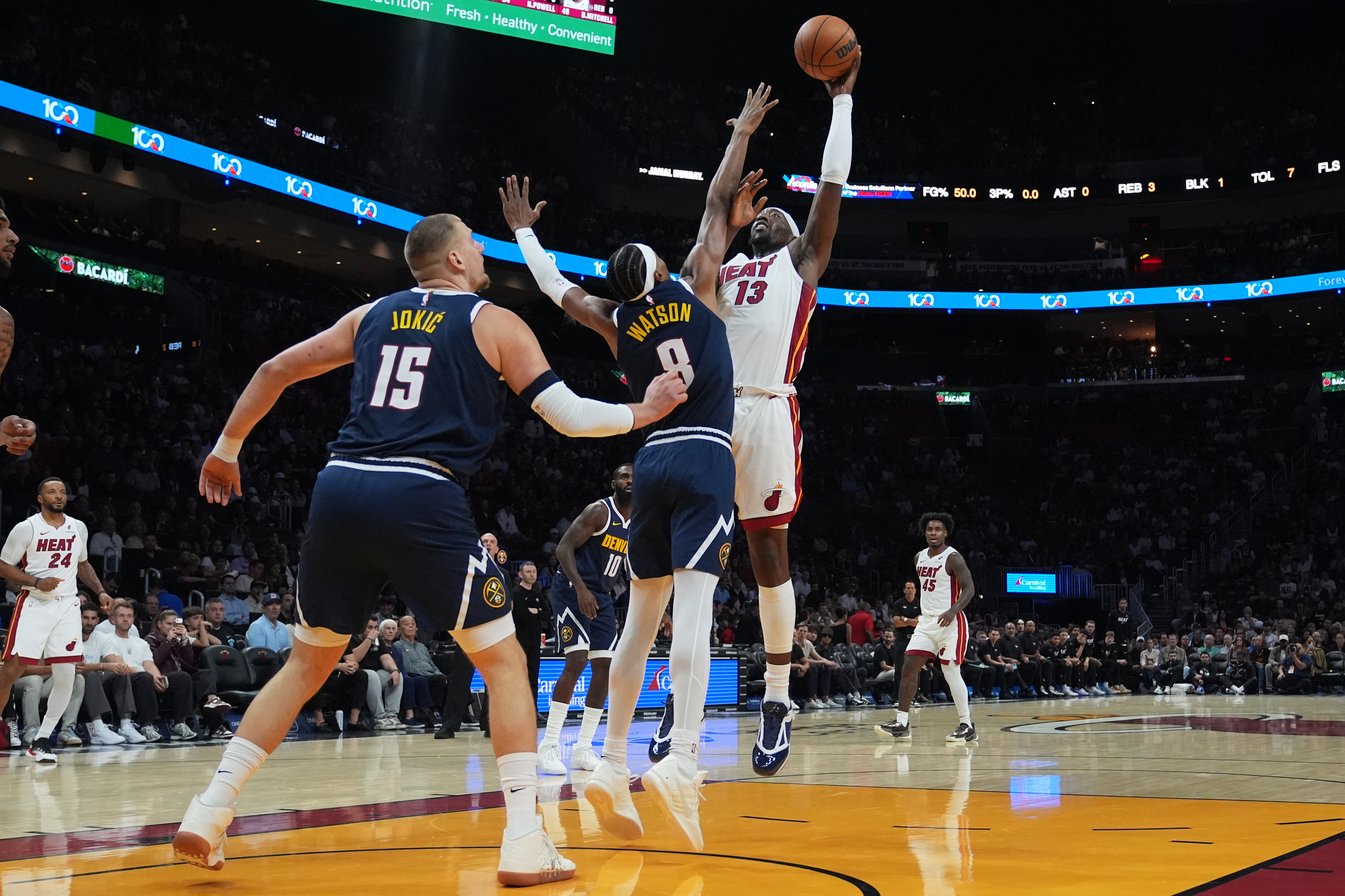 Miami Heat center Bam Adebayo (13) shoots as Denver Nuggets center Nikola Jokic (15) and guard Peyton Watson (8) defend during the first half of an NBA basketball game, Monday, Dec. 29, 2025, in Miami.