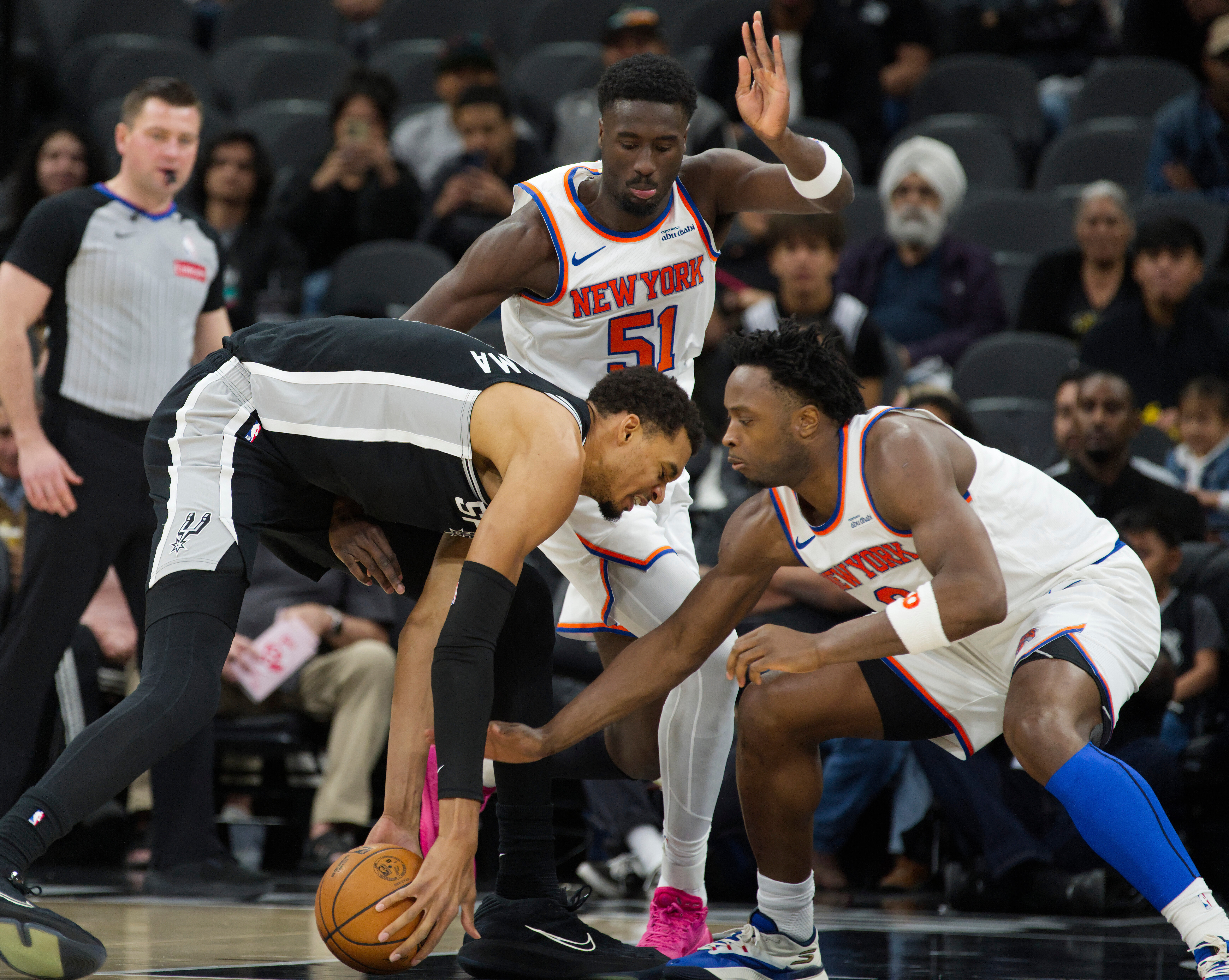 San Antonio Spurs center Victor Wembanyama, left, tangles with New York Knicks players Mohamed Diawara and OG Anunoby during the first half of an NBA basketball game, Wednesday, Dec. 31, 2025, in San Antonio.