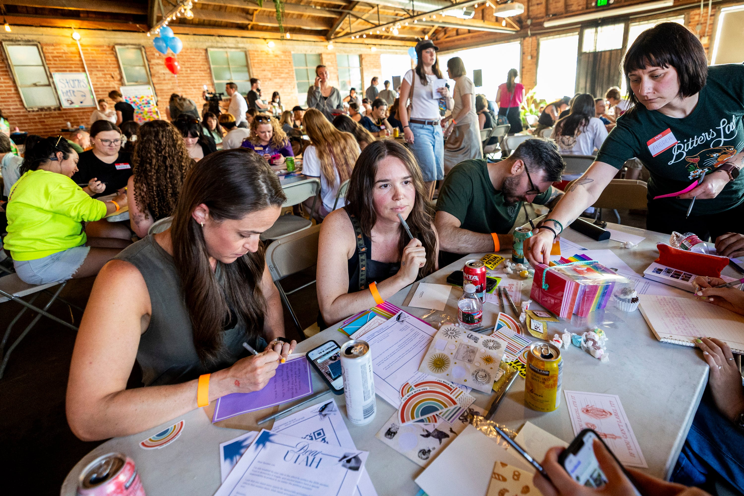 Sydney Shine, of Millcreek, listens to a friend as her husband, Matt Shine, and Jenn Delman, of Draper, write letters to Sen. Mike Lee, R-Utah, during a letter-writing event to hold Sen. Lee accountable, hosted by the Alliance for a Better Utah and Elevate Utah, held at Publik Coffee Roasters in Salt Lake City on June 25, 2025. Lee came under fire for including public lands proposals in President Donald Trump's signature tax and spending bill.