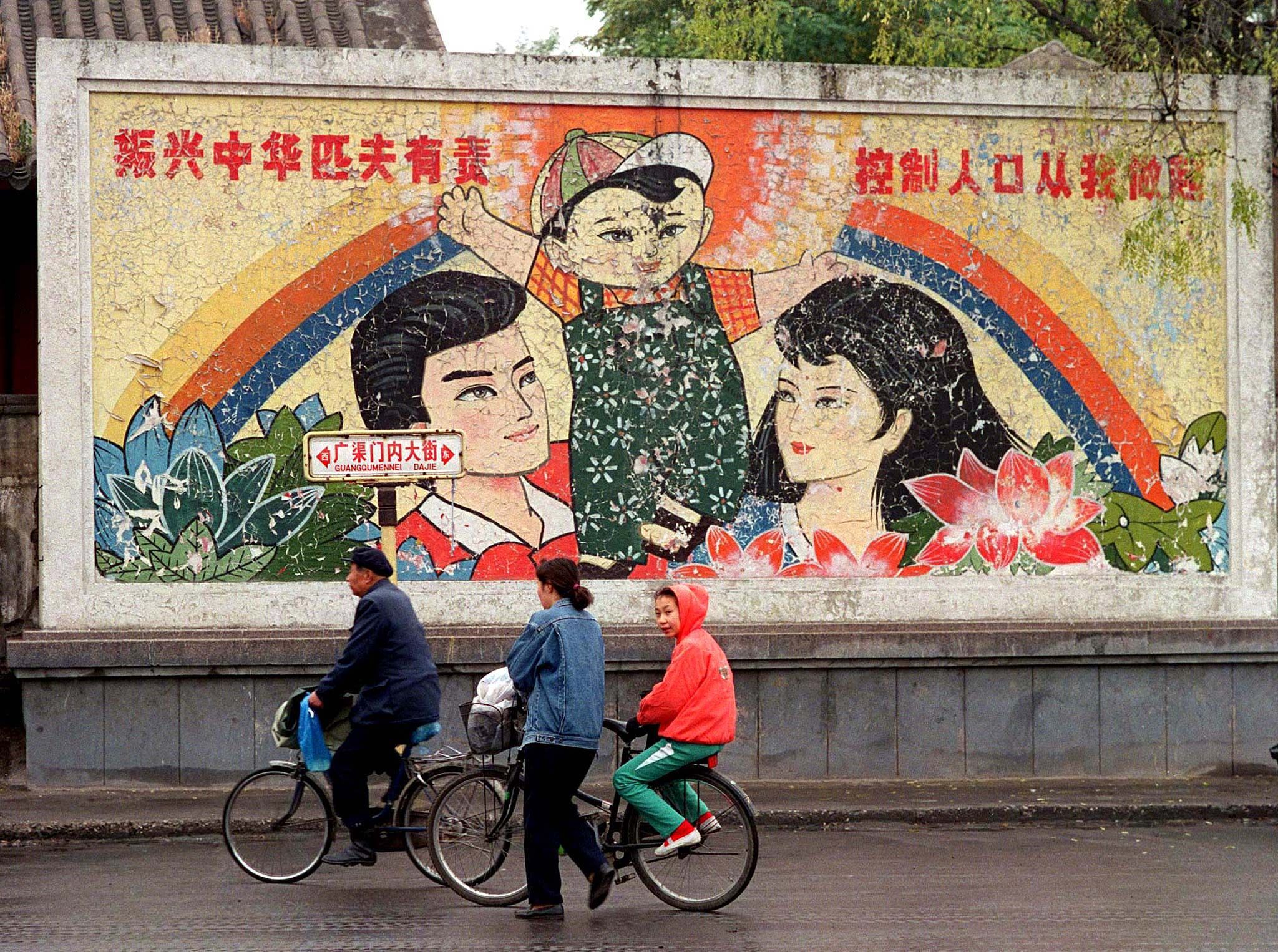 People cycle past a mural promoting the "one-child" policy on a Beijing street in 1996.