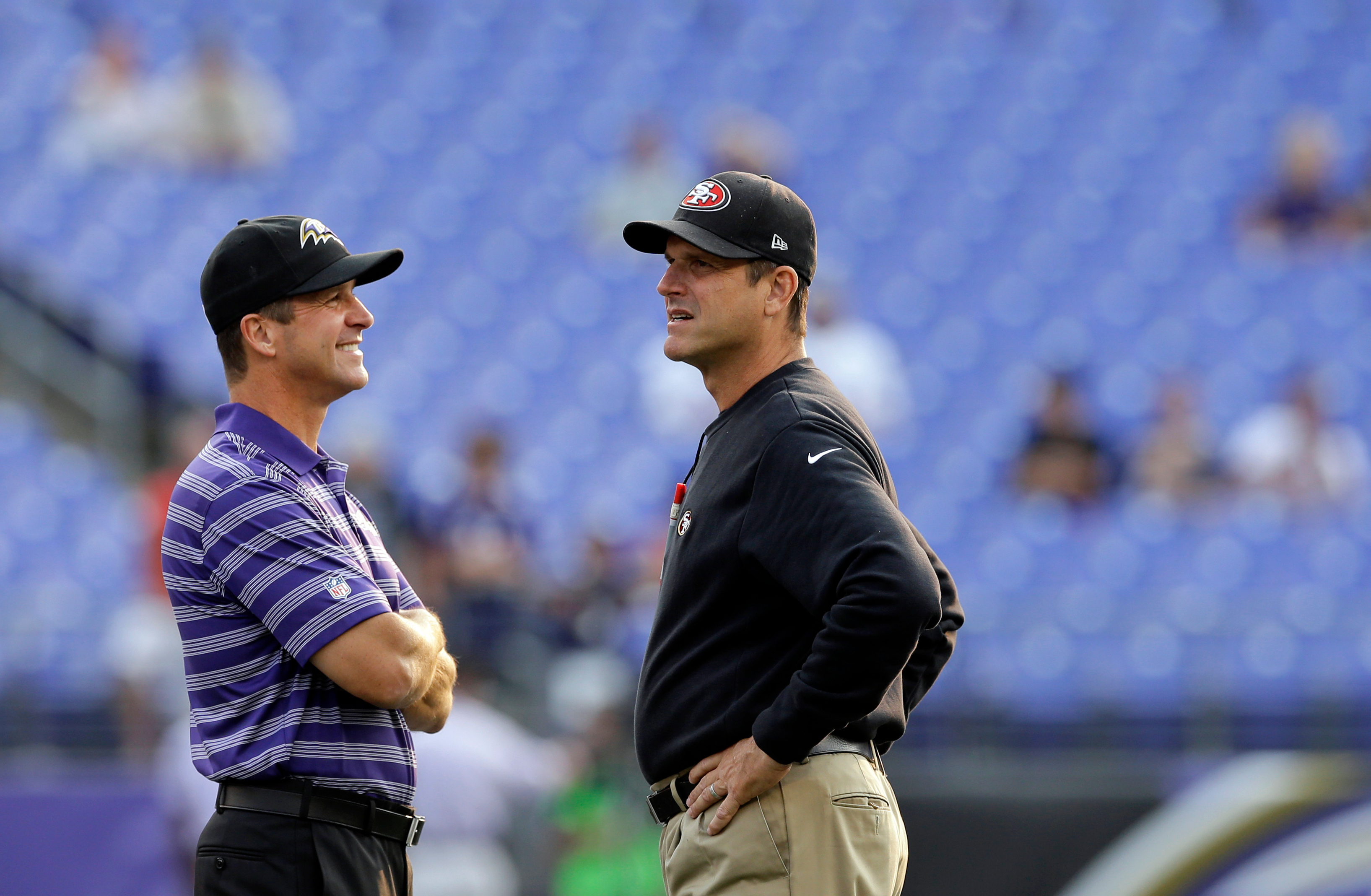 FILE - Baltimore Ravens head coach John Harbaugh, left, and San Francisco 49ers head coach Jim Harbaugh chat before an NFL preseason football game, Aug. 7, 2014, in Baltimore.