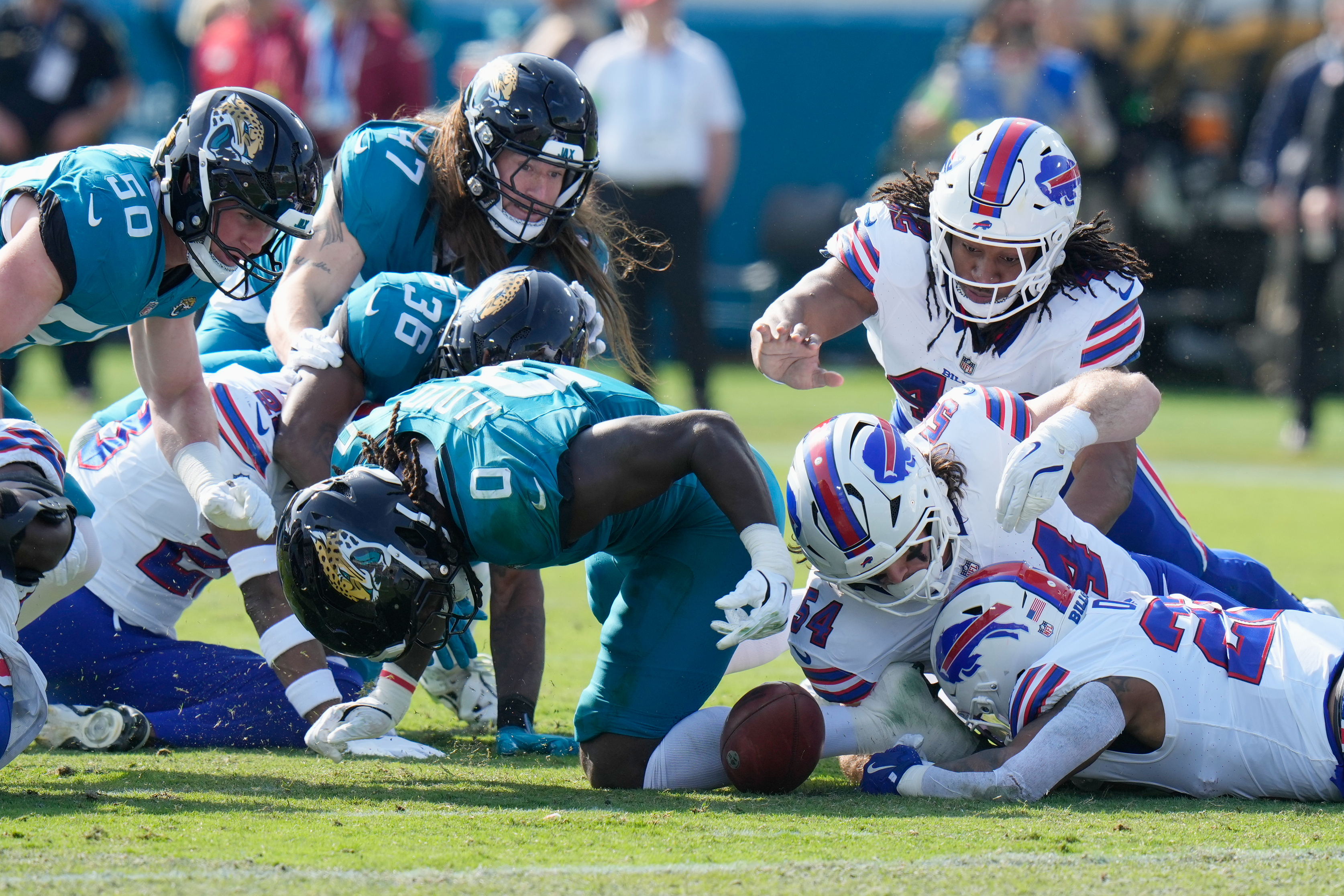 Buffalo Bills' Ray Davis, bottom right, fumbles a kickoff return from the Jacksonville Jaguars as teammate Baylon Spector (54) and Jacksonville Jaguars' Devin Lloyd (0) try to recover the ball during the first half of an NFL wild-card playoff football game Sunday, Jan. 11, 2026, in Jacksonville, Fla.