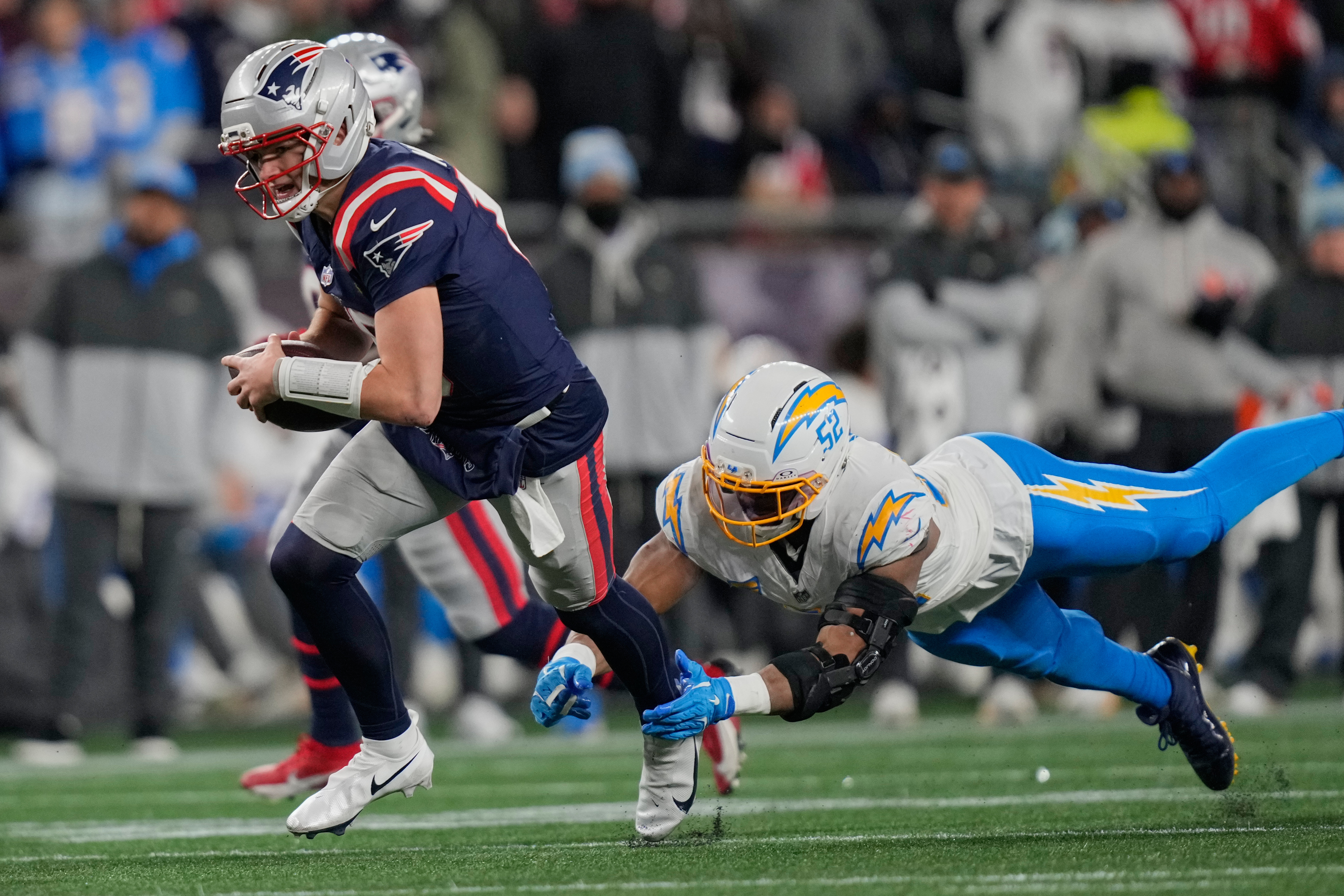 New England Patriots quarterback Drake Maye, left, avoids a tackle by Los Angeles Chargers linebacker Khalil Mack (52) in the second half of an NFL wild-card playoff football game in Foxborough, Mass., Sunday, Jan. 11, 2026.