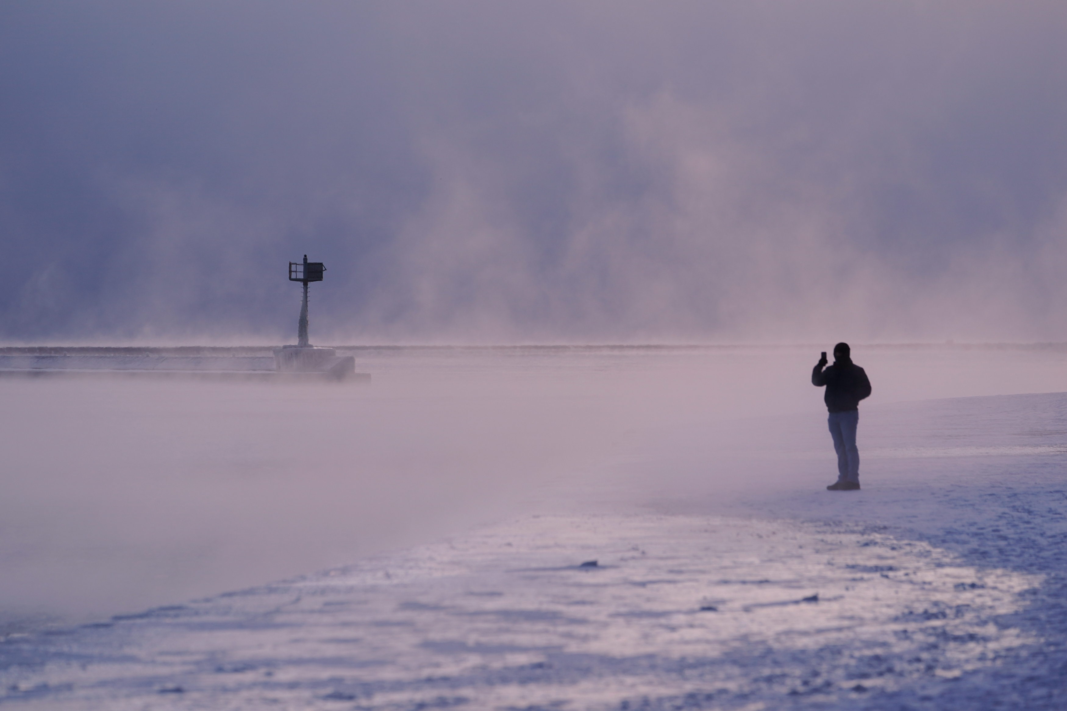 A person walks on an ice covered beach along the shore of Lake Michigan, Friday, in Chicago. While extreme cold is a concern coast to coast, the Northeast could see its heaviest snow in years.