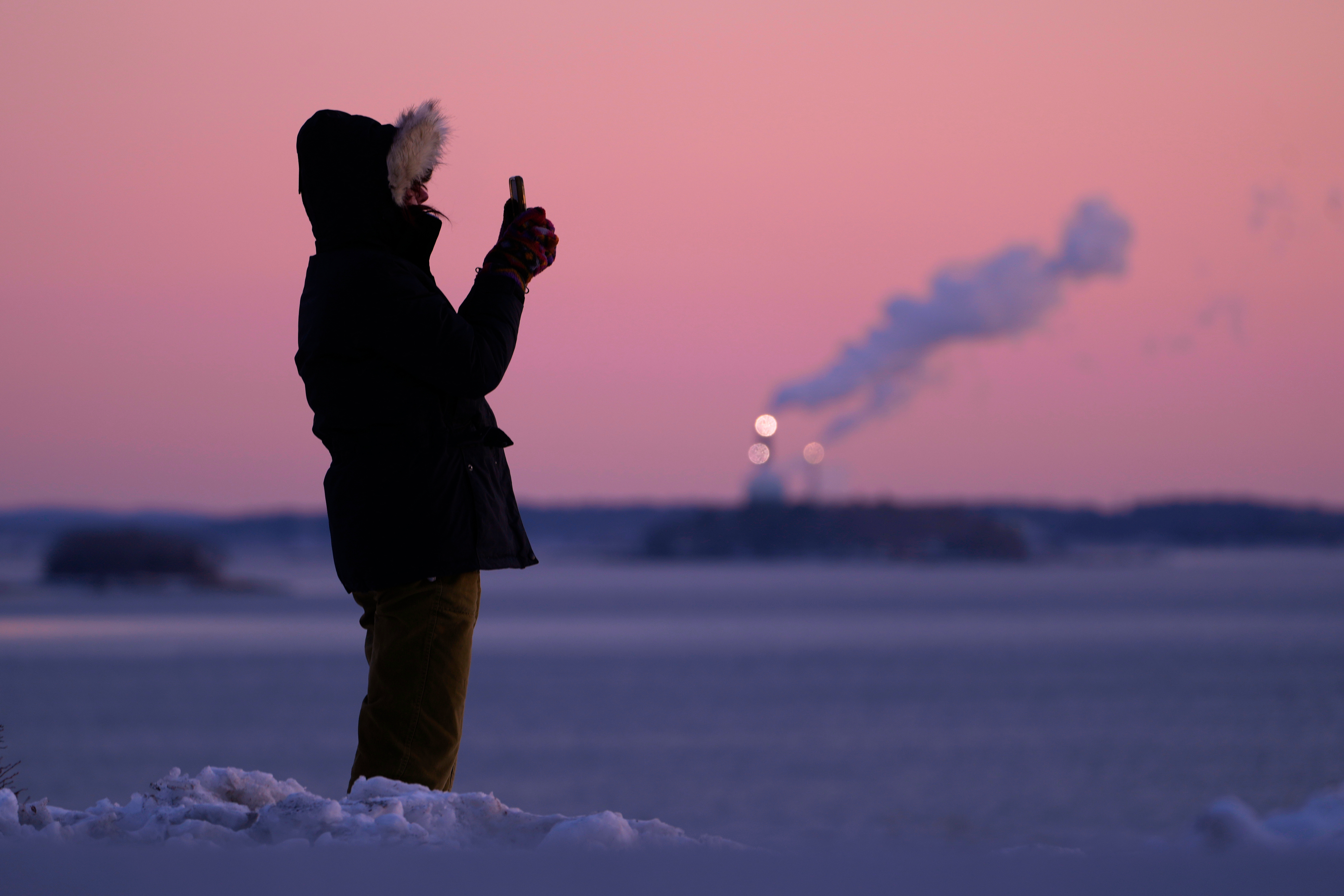 Emma Nadeau, of North Yarmouth, Maine, photographs the pre-dawn scene overlooking Casco Bay on a 1-degree morning, Saturday, in Portland, Maine, as a major winter storm upended travel across the nation.