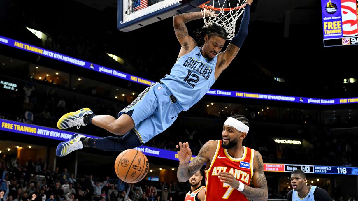 Memphis Grizzlies guard Ja Morant (12) hangs from the rim after dunking against Atlanta Hawks guard Nickeil Alexander-Walker (7) in the second half of an NBA basketball game Wednesday, Jan. 21, 2026, in Memphis, Tenn.