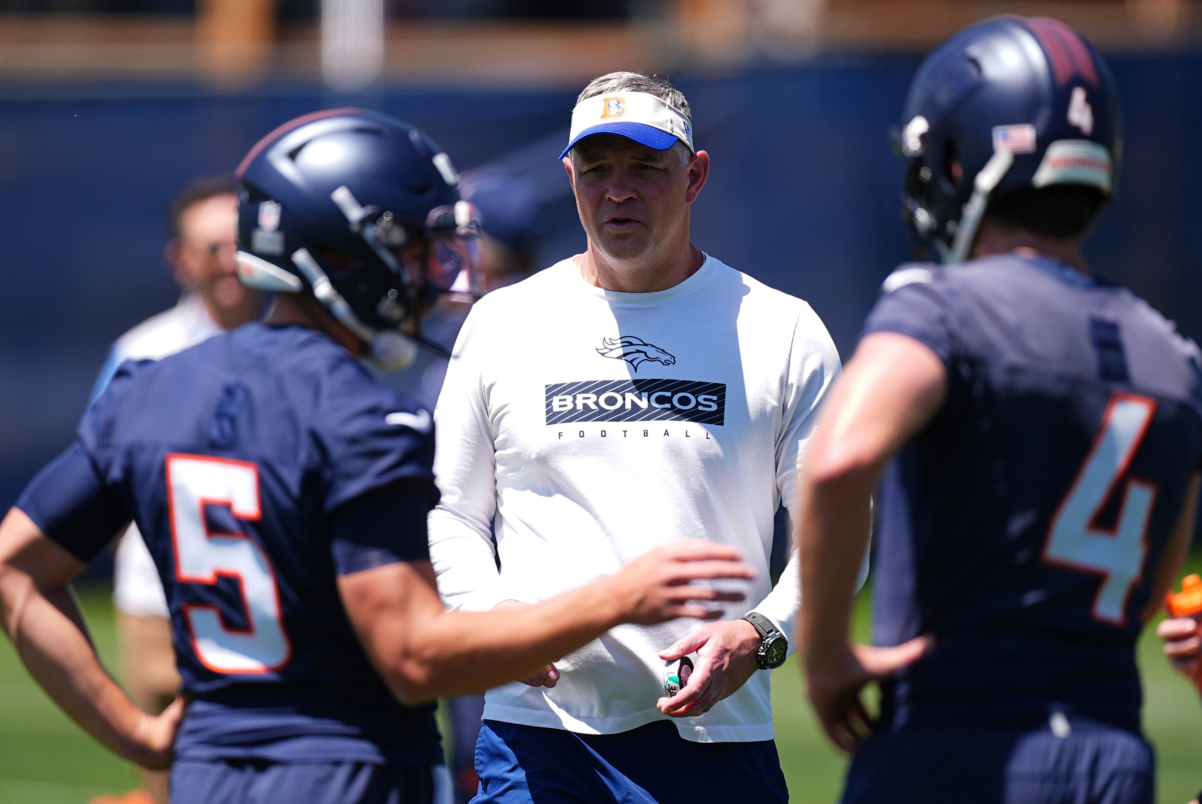 FILE - Denver Broncos offensive coordinator Joe Lombardi, center, confers with Denver Broncos quarterbacks Ian Book (5) and Blake Stenstrom (4) as they take part in drills during the NFL football team's rookie minicamp, May 10, 2025, in Centennial, Colo. 